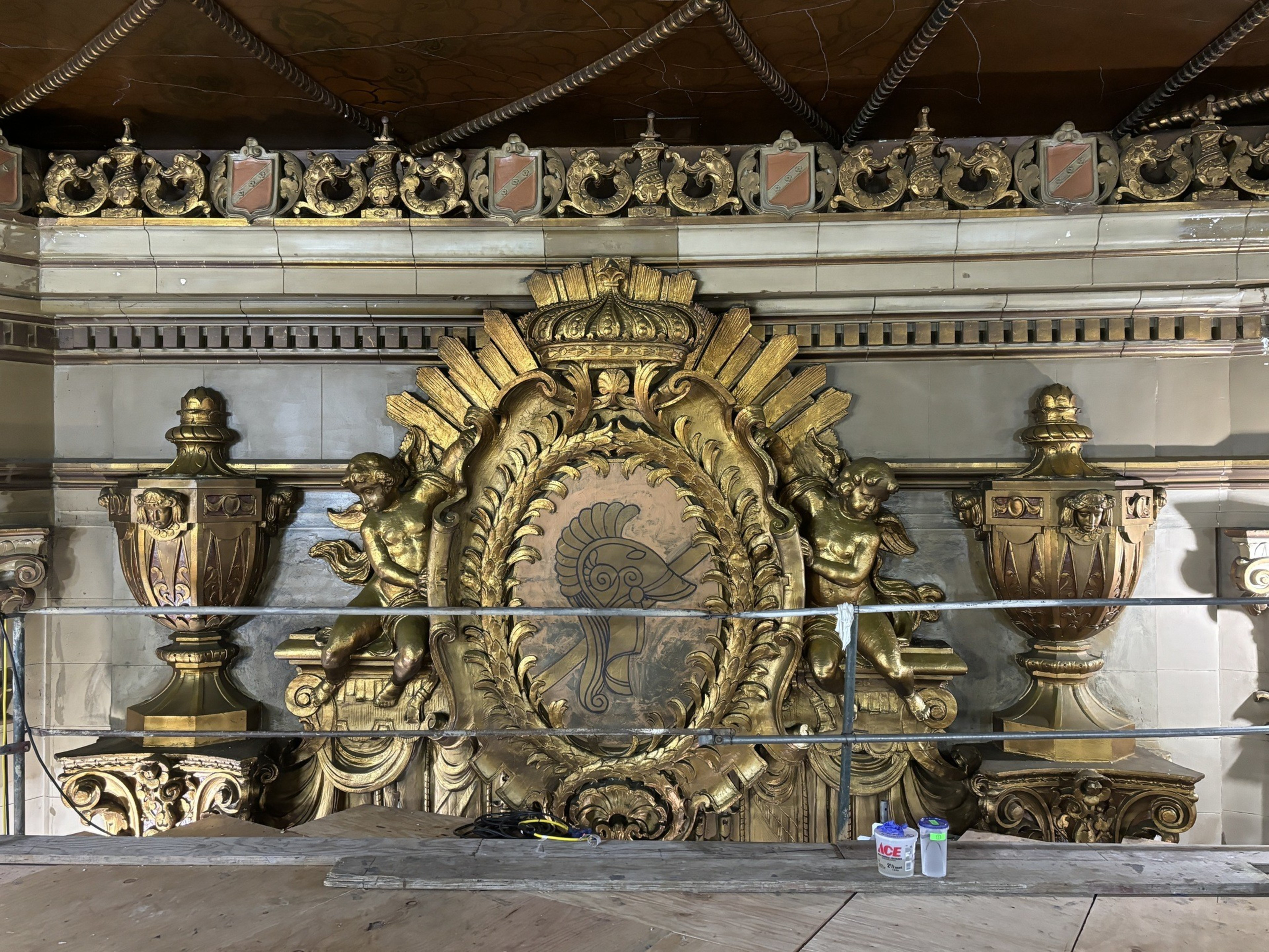 a close-up shot of a gold leaf-covered section of the upper wall, with cherub-like angels flanking a decorative shield