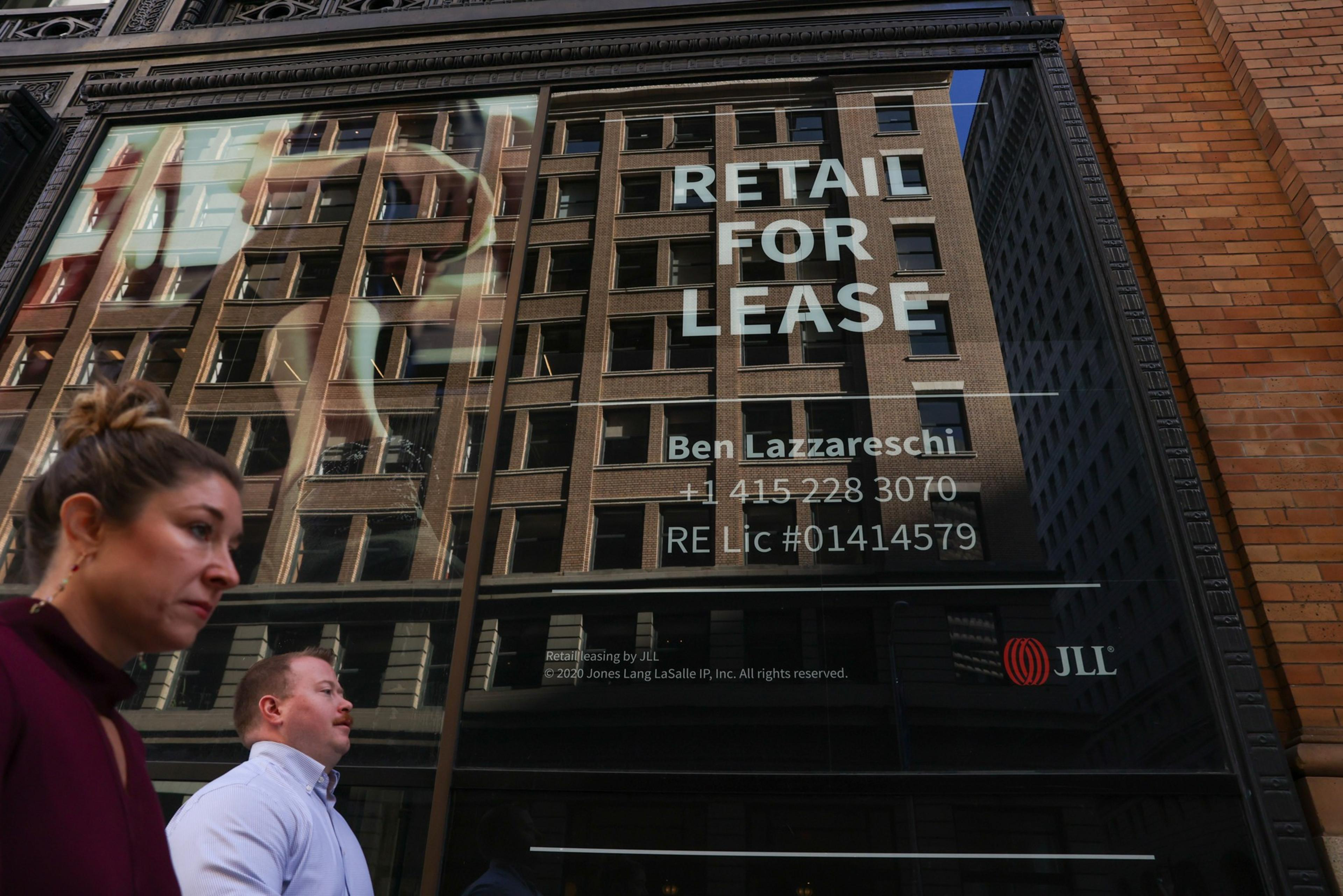 A glass window displays "RETAIL FOR LEASE" with contact details, reflecting a tall building; a woman and man walk past below the sign.