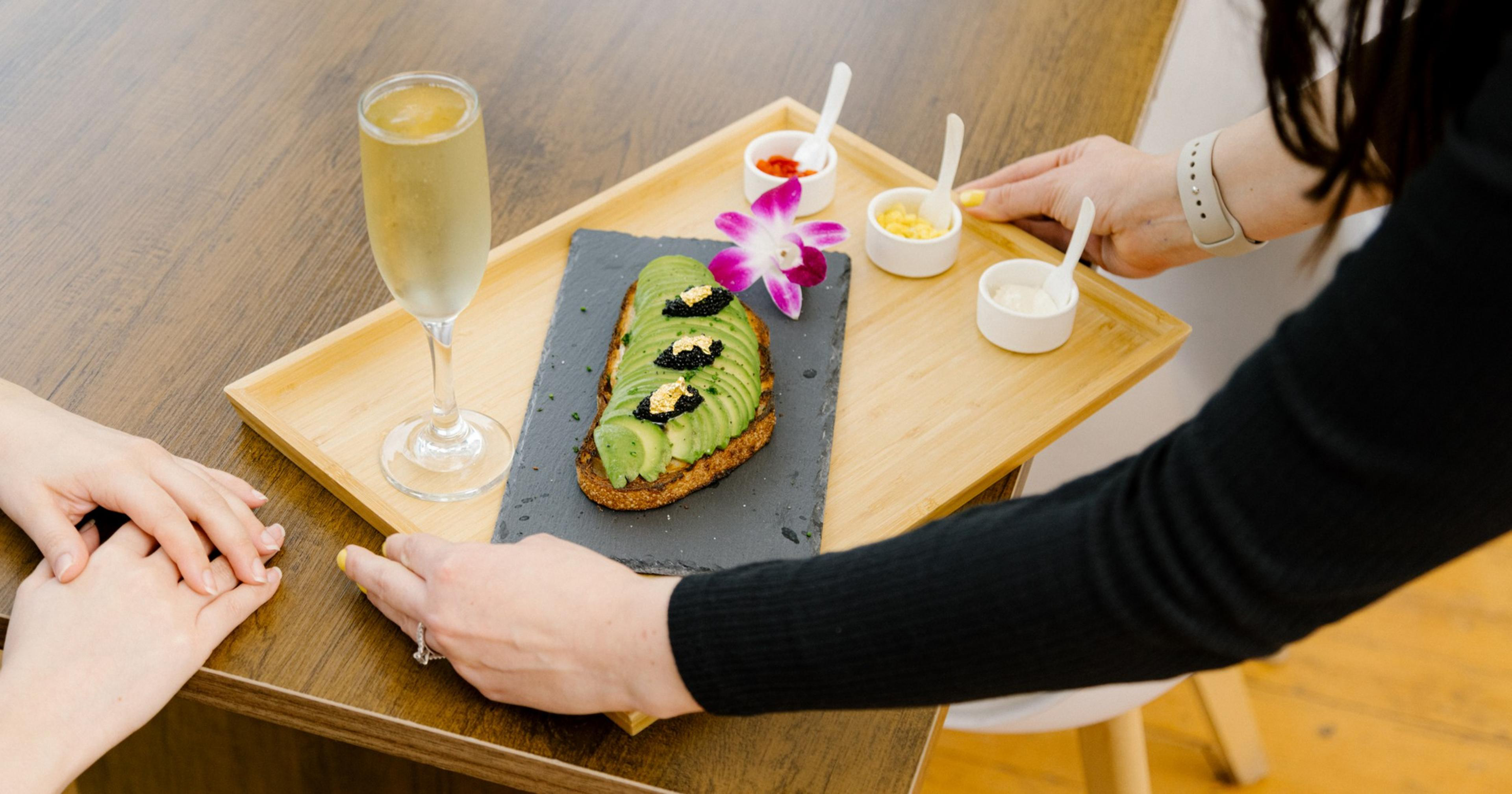 Avotoasty owner Sofia Pinzon serves a tray of the $50 avocado toast topped with edible gold leaf and caviar and served with a glass of champagne.