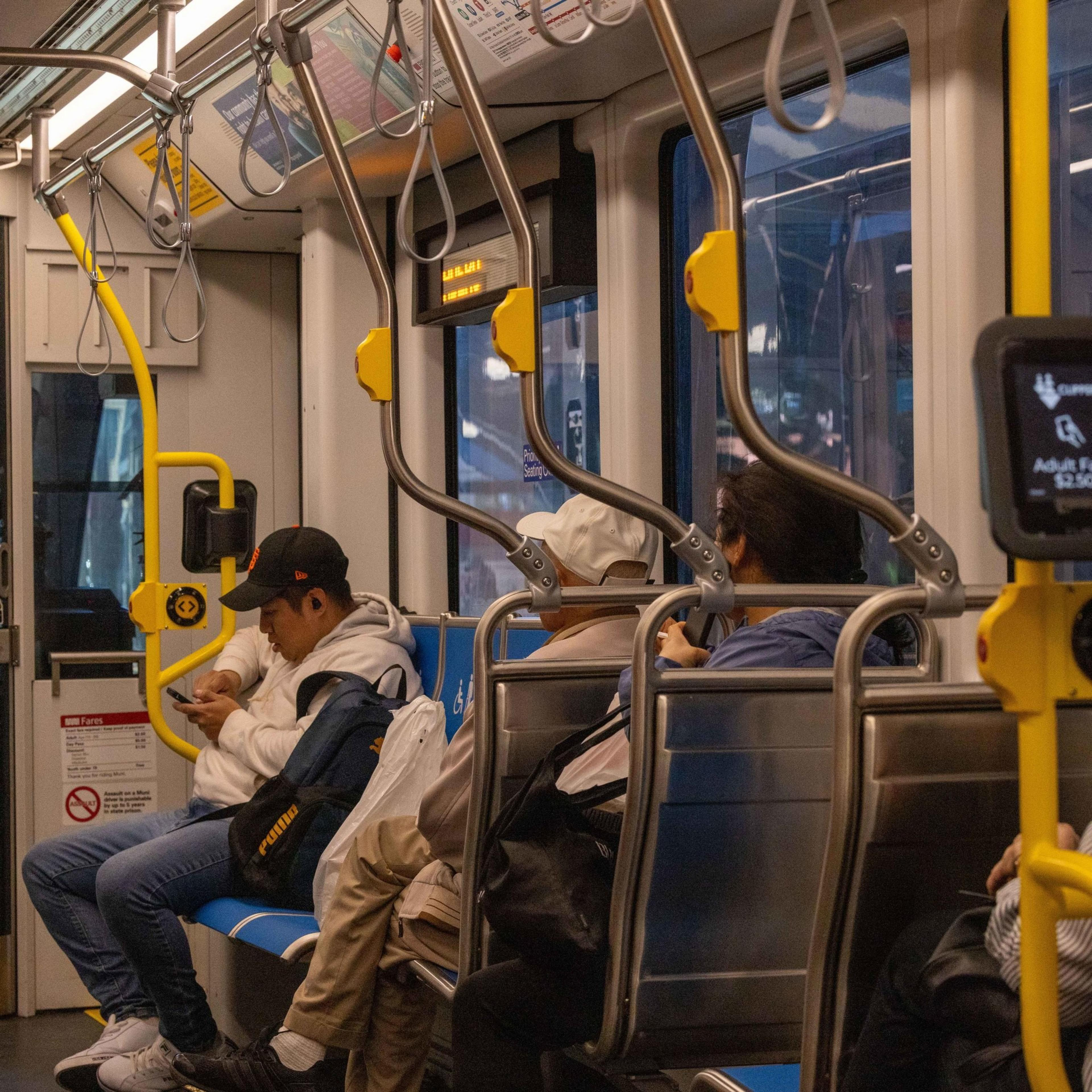 Three passengers sit in a bus, with one person focused on their phone, while the others look ahead.