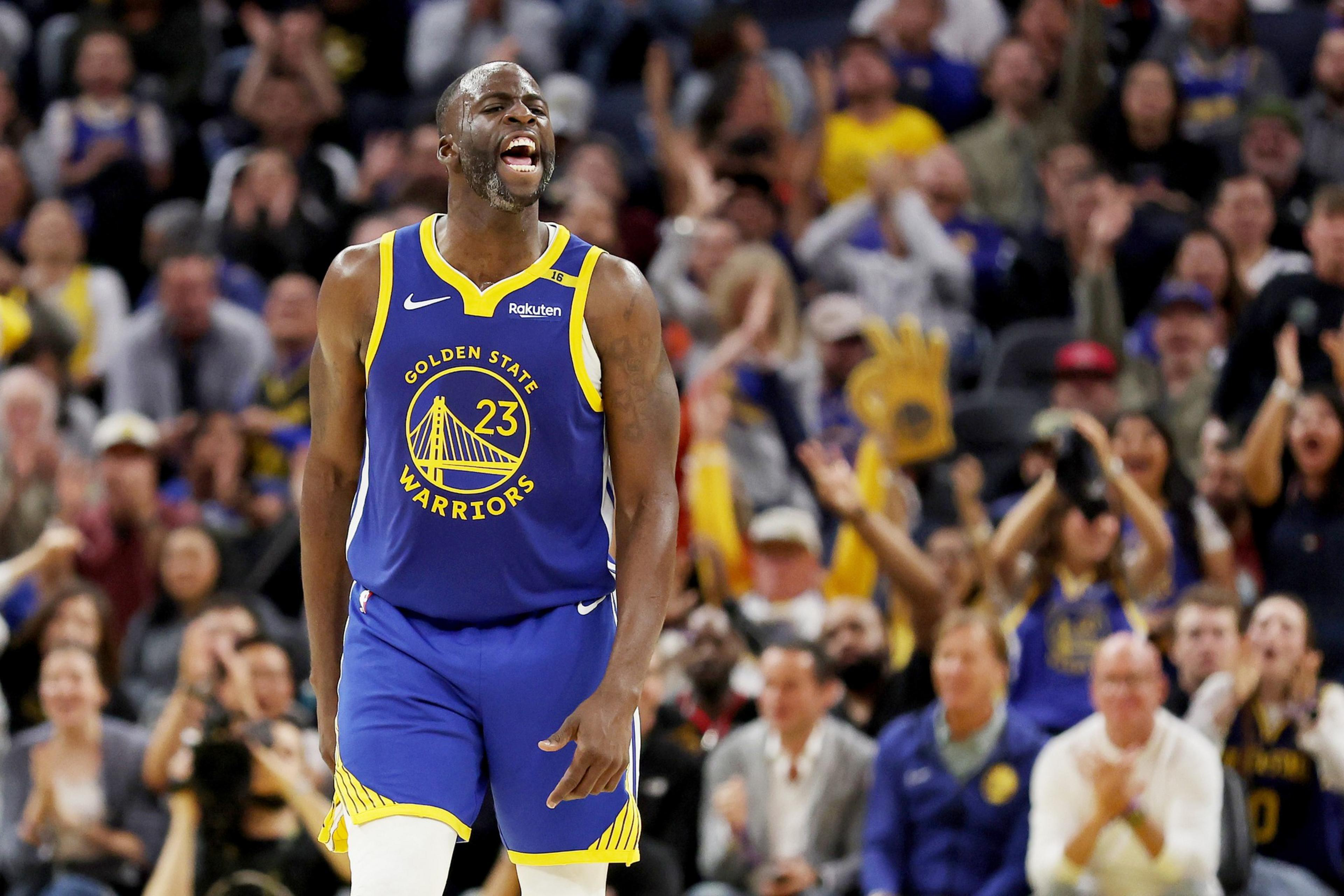 A basketball player in a Golden State Warriors jersey is on the court, yelling in excitement. The crowd behind him is cheering enthusiastically.