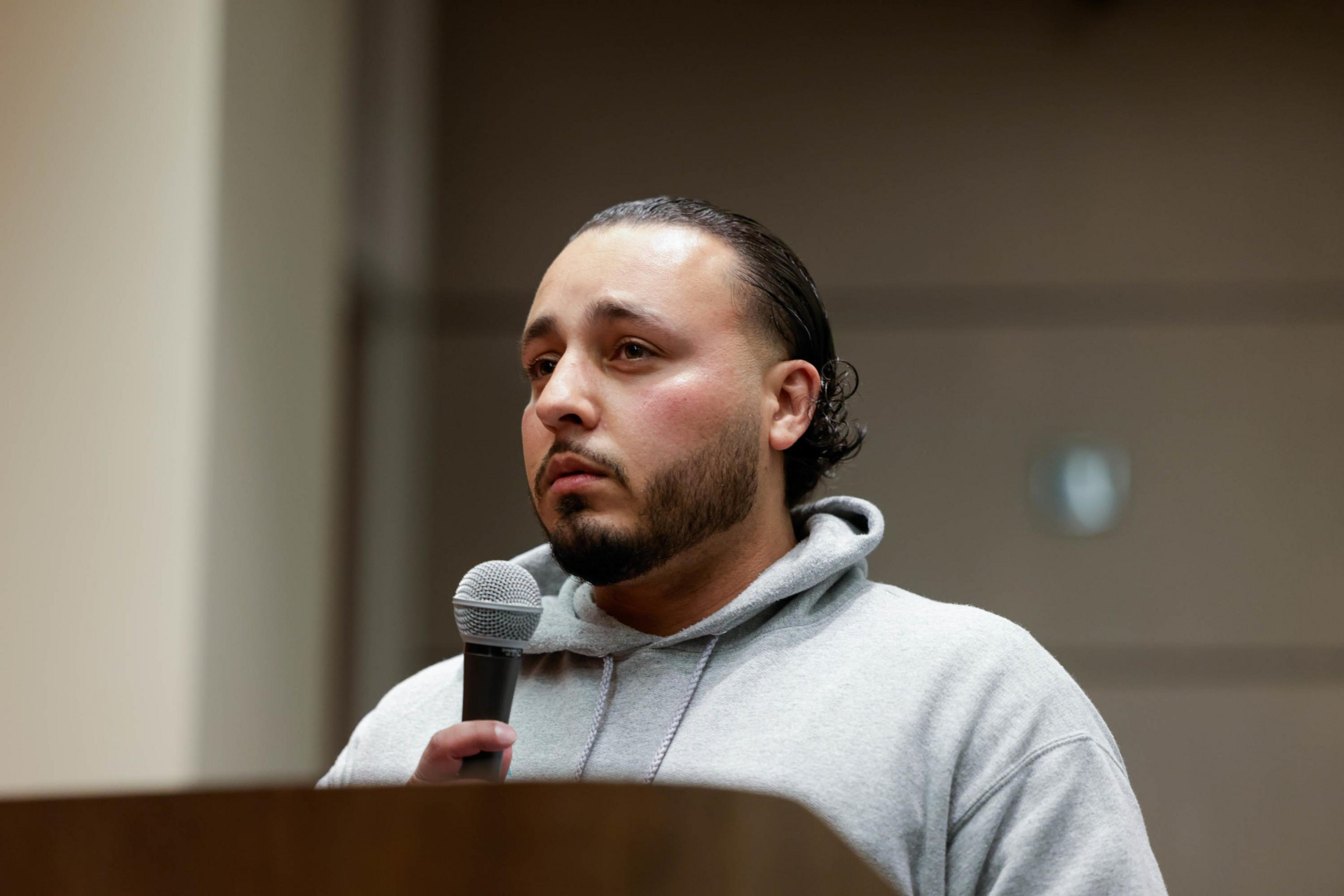 A man in a hoodie speaks at a podium.