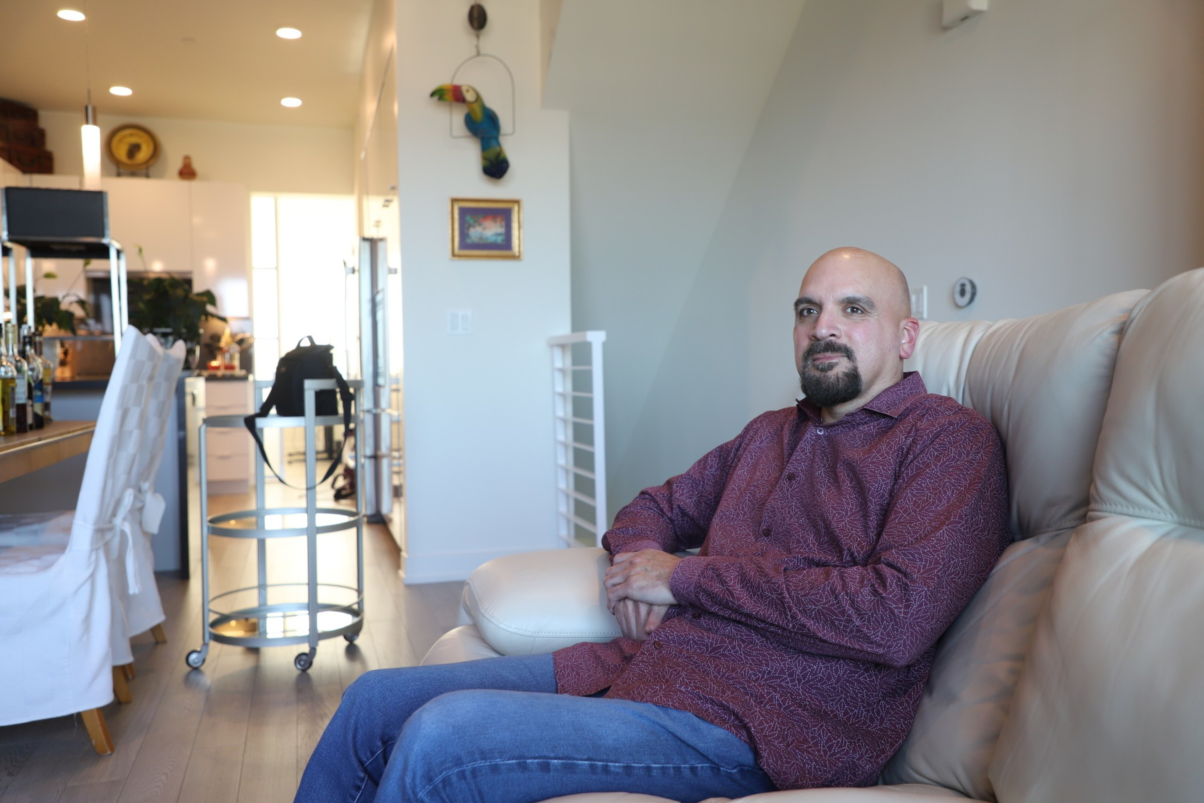 A man sits on a couch inside his home.