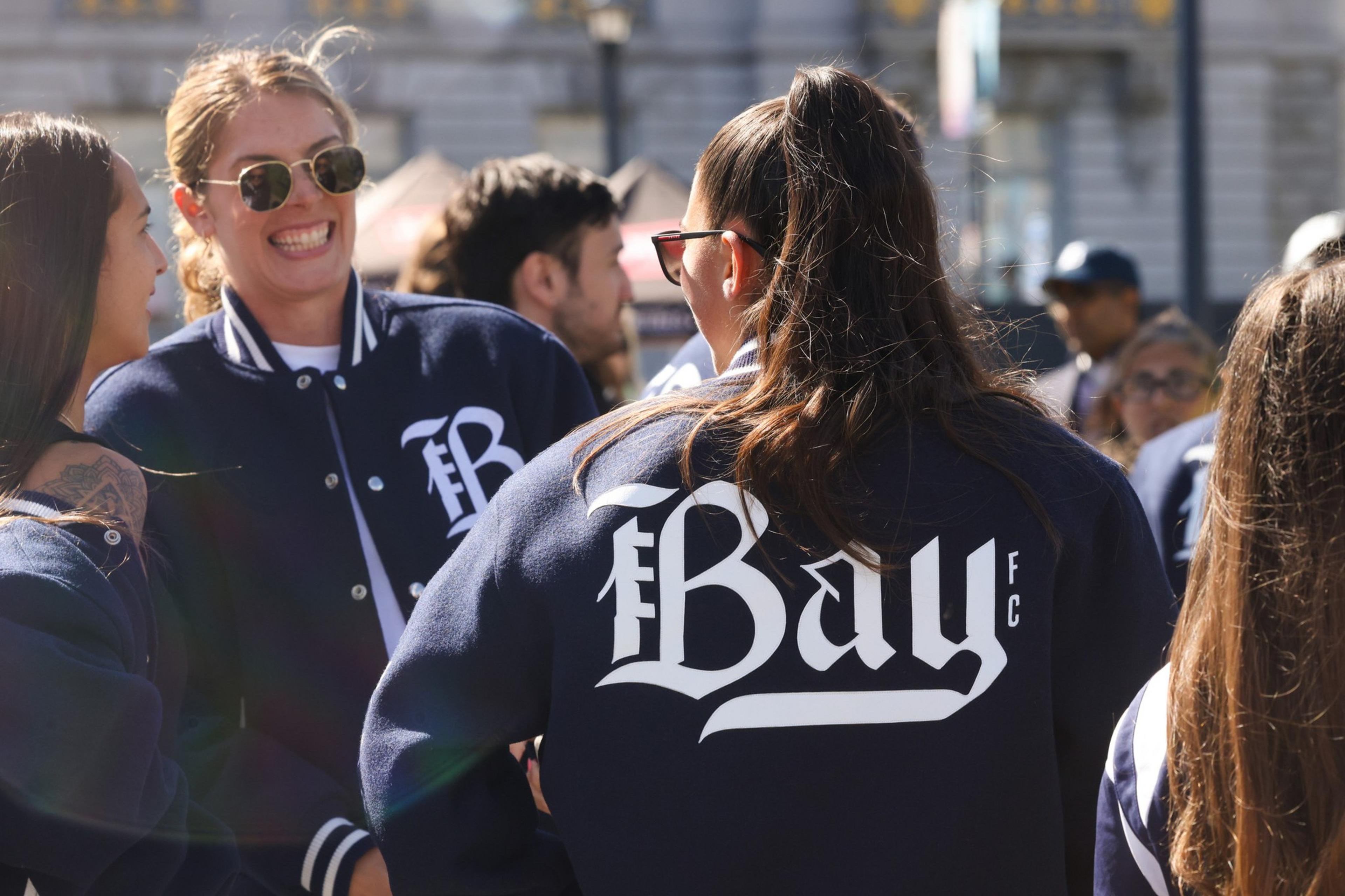 A group of people in a crowd, one wearing a jacket with "The Bay" printed on the back.