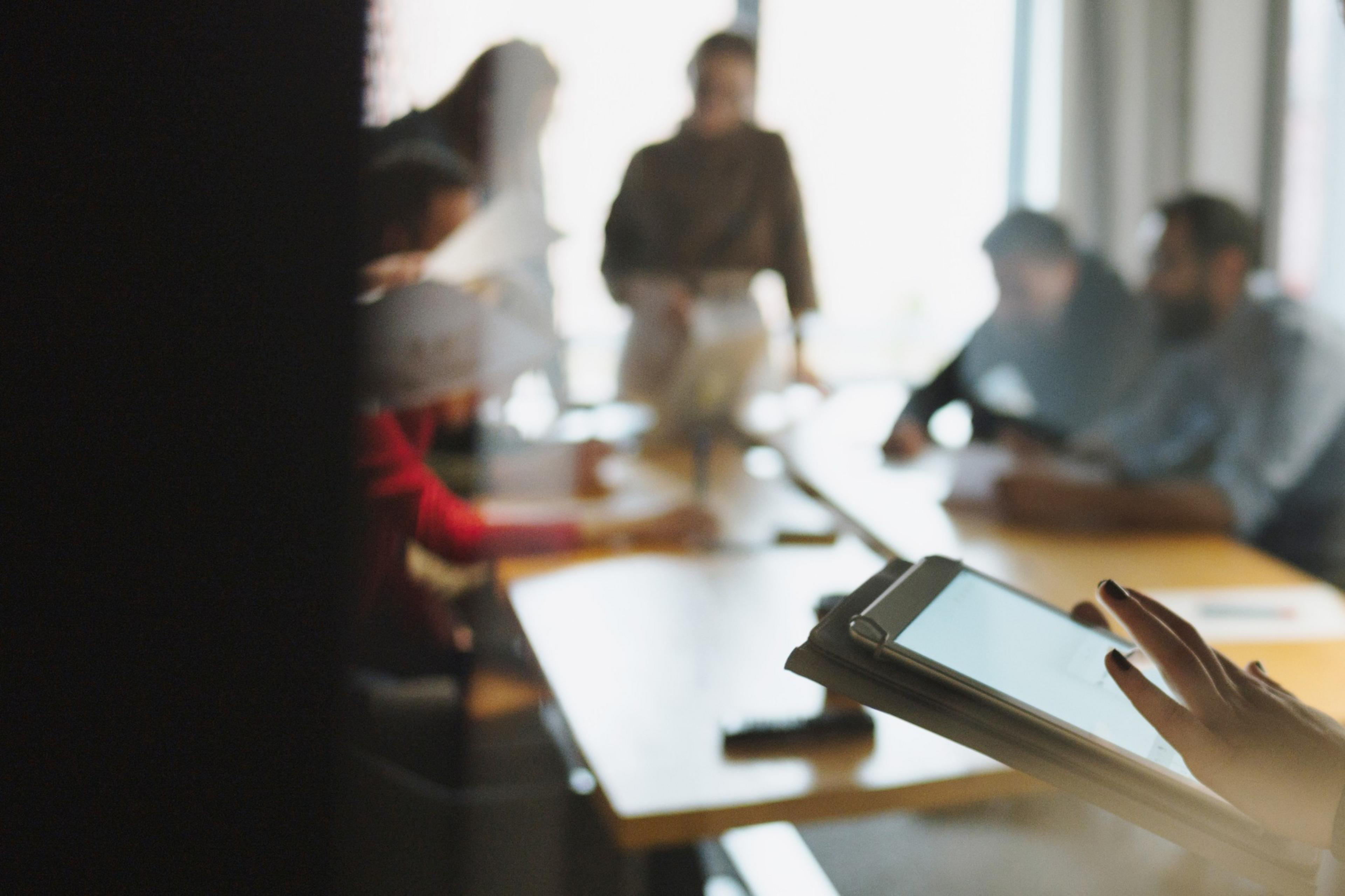 A blurred view through a glass window of people sitting inside a conference room