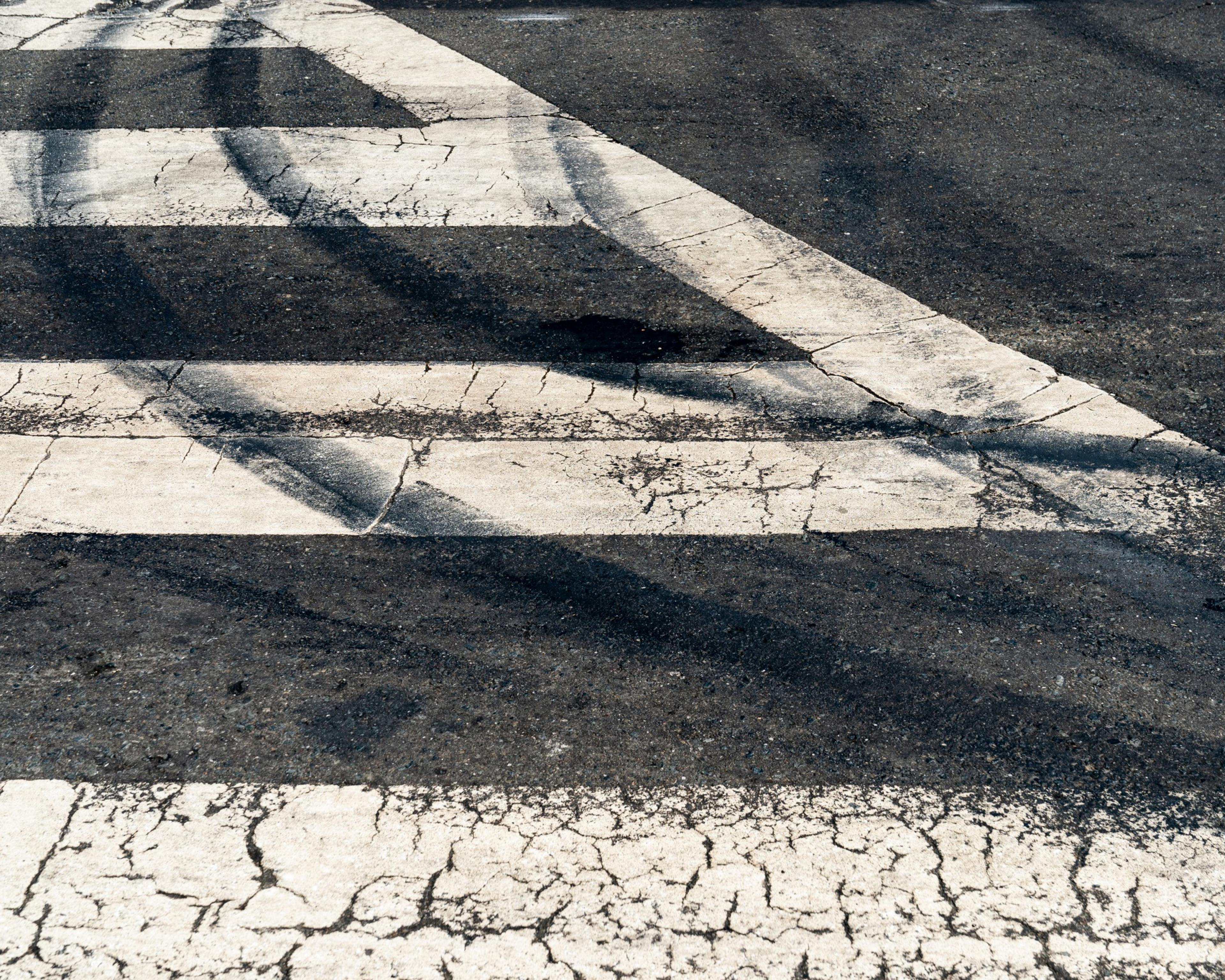 A crosswalk with white stripes on an asphalt road is shown. The surface is weathered and has multiple black tire skid marks crossing the white lines.