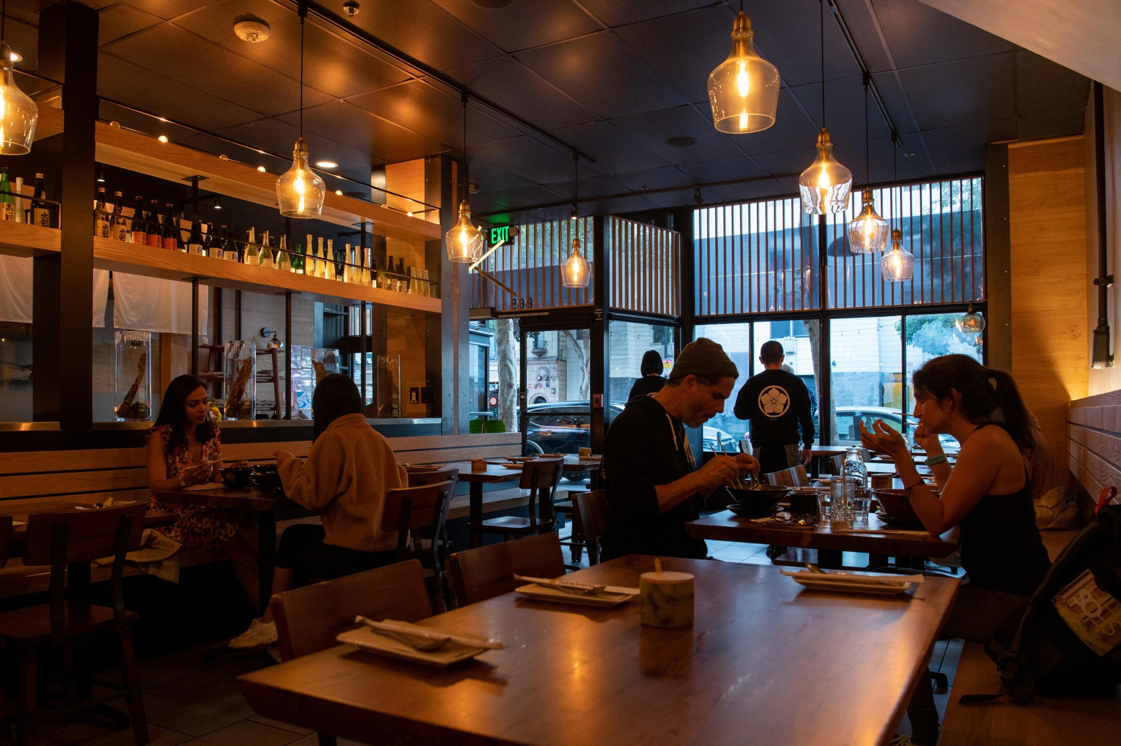 A handful of patrons sit and talk at tables in a dimly lit restaurant.