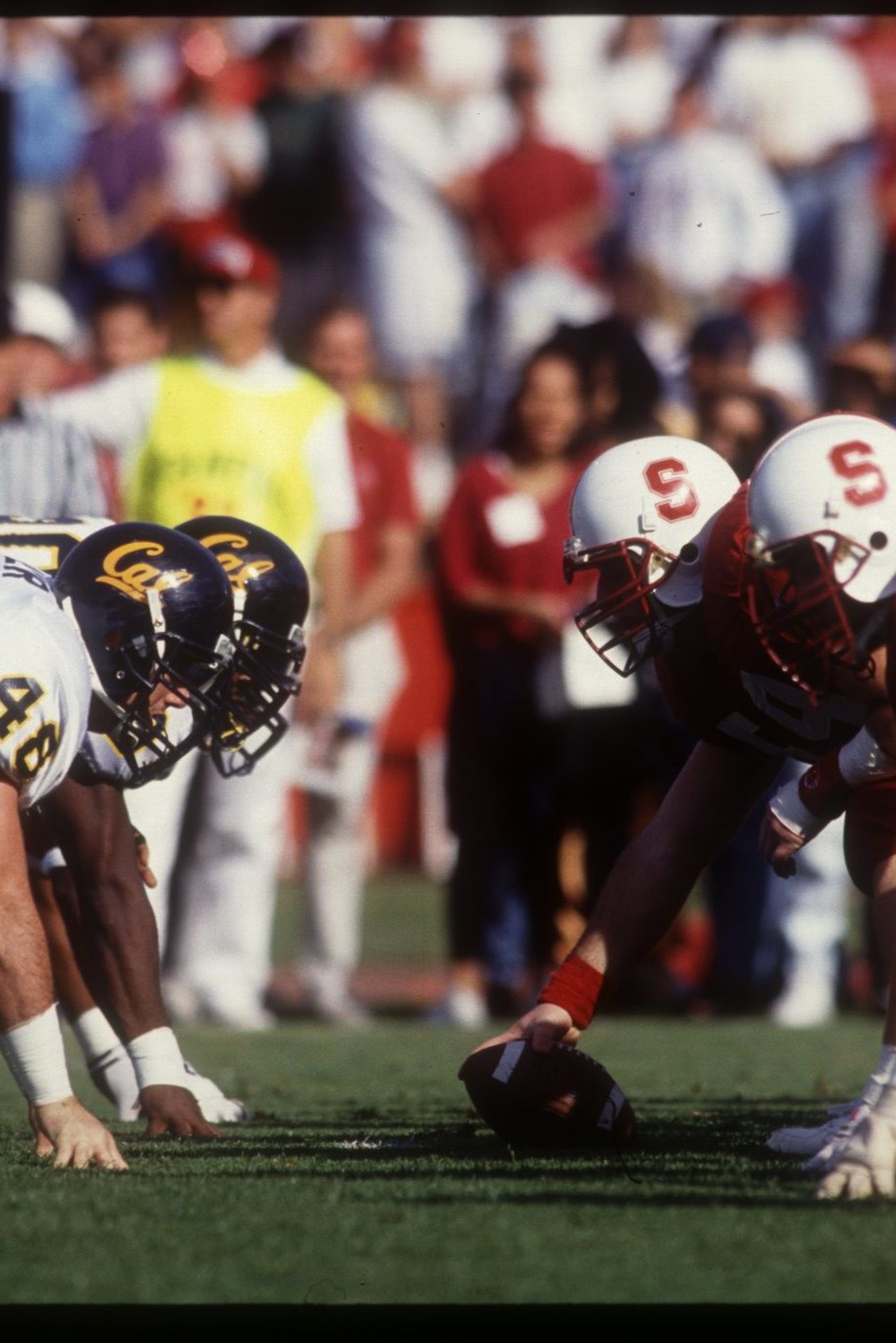 Two American football teams, one in white and navy and the other in red and white, face off on the line of scrimmage, ready for the snap.