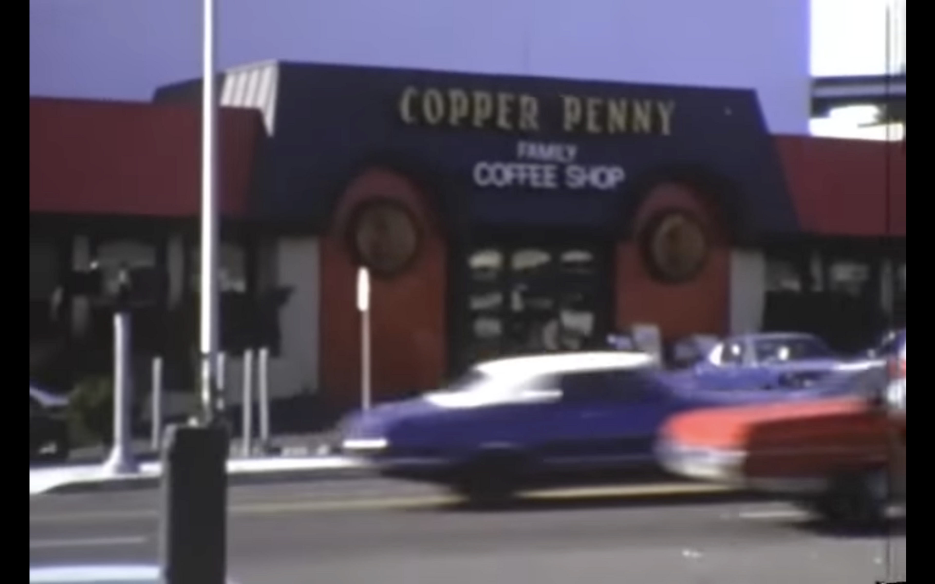 A blurred image of a coffee shop named &quot;Copper Penny&quot; with passing cars in front.