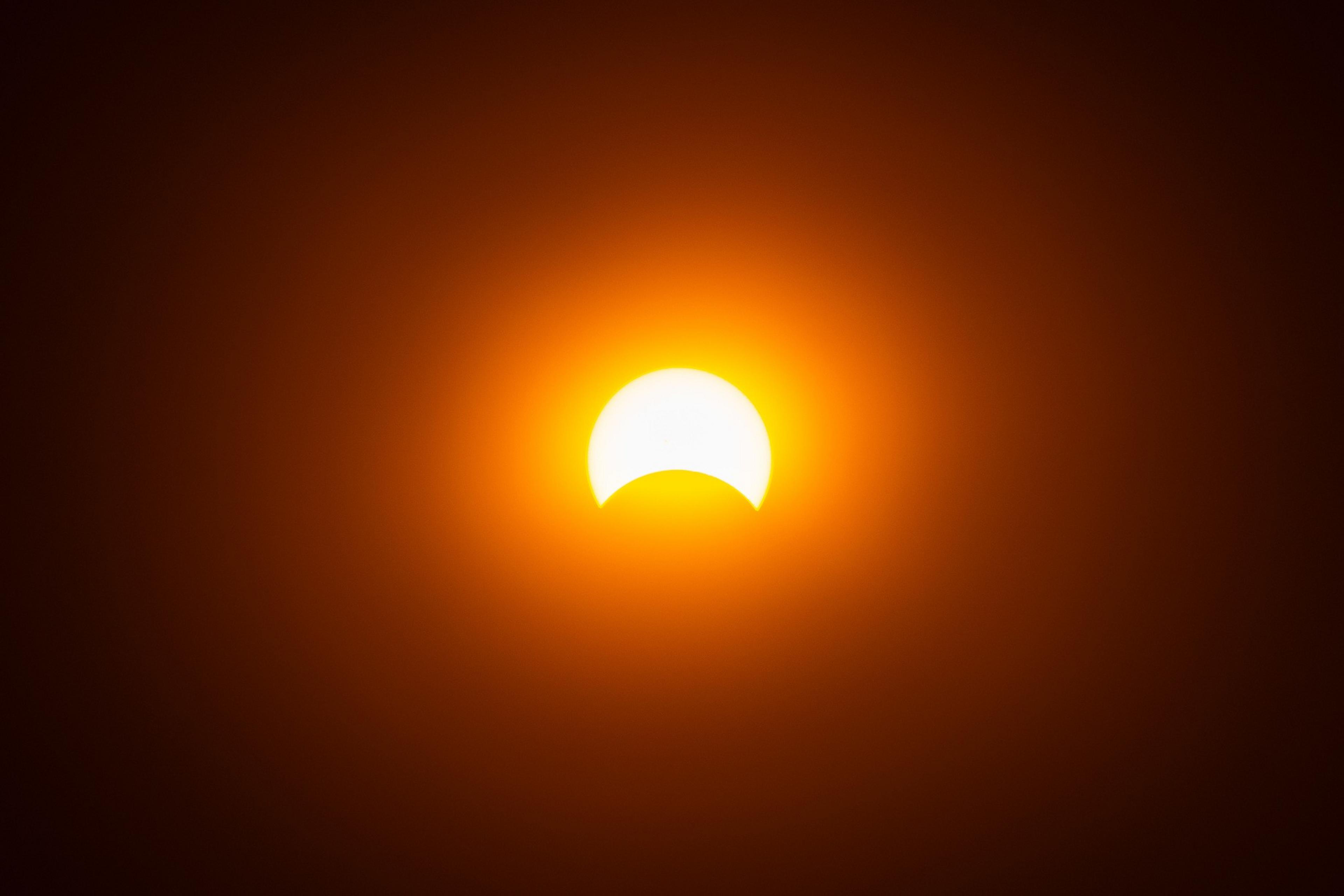 A solar eclipse; the Moon partially covers the Sun, against an orange sky.