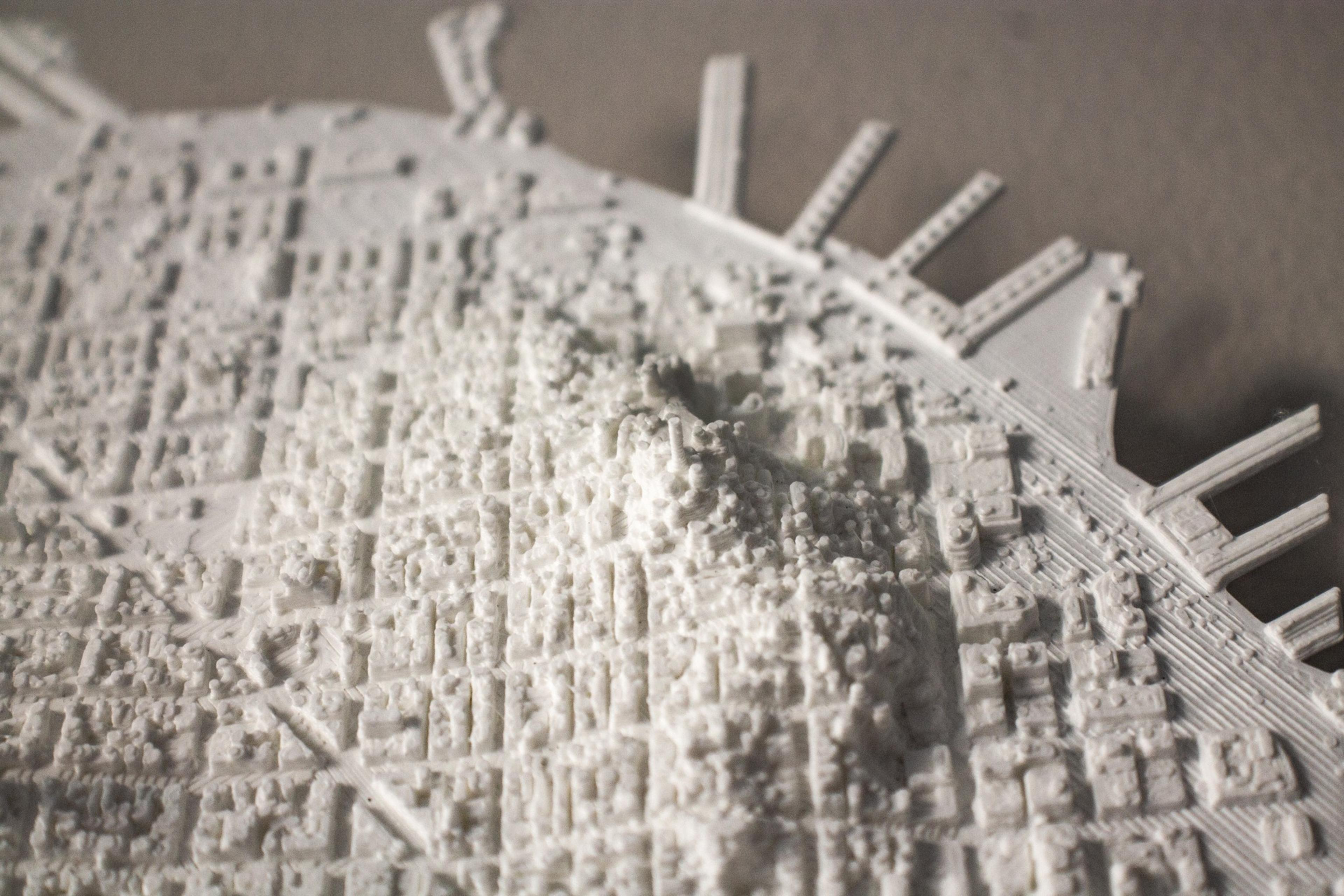 A detailed white 3D model of a cityscape including buildings, streets, elevated terrain, and waterfront piers is shown in close-up.