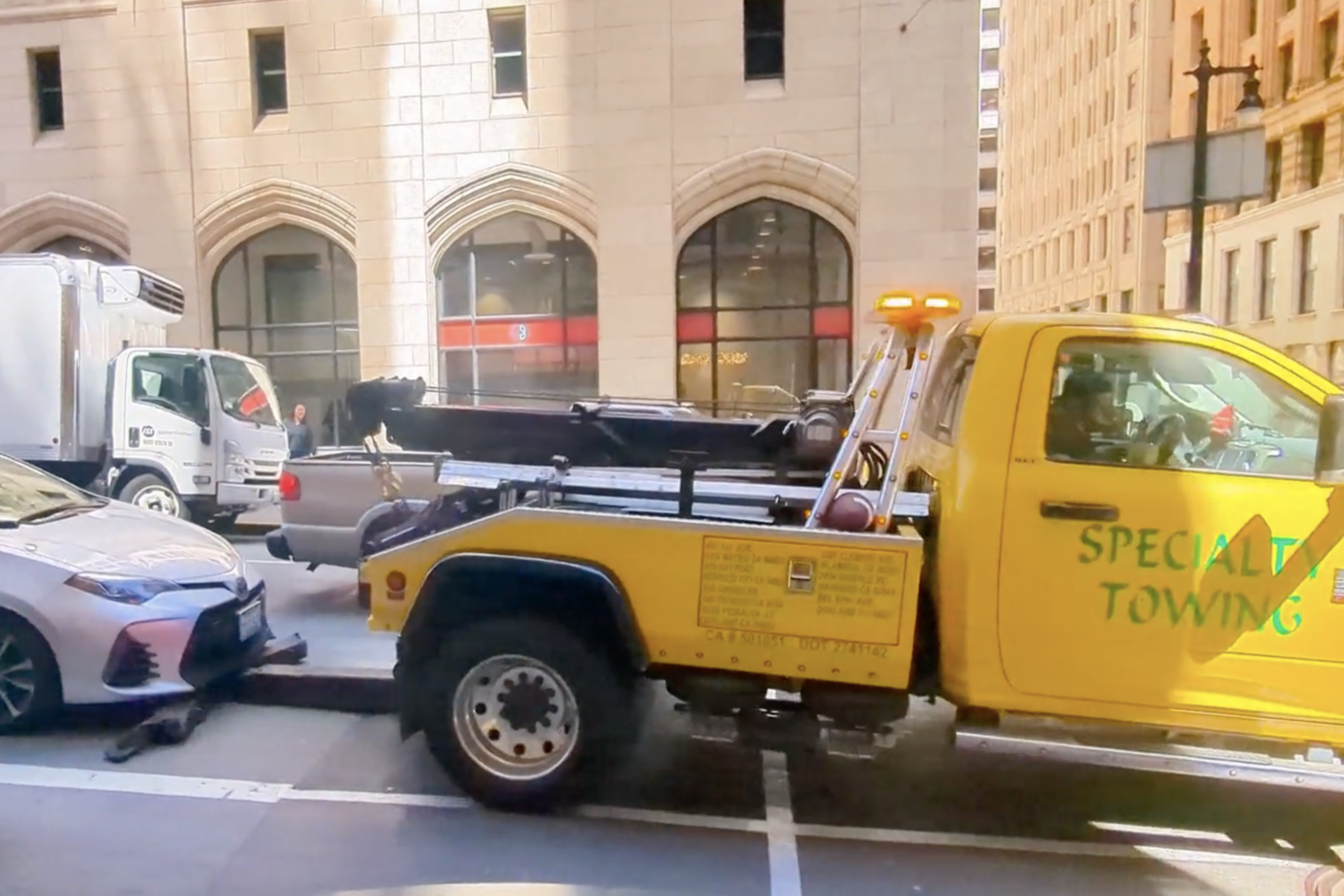 a yellow tow truck attempts to tow a silver sedan