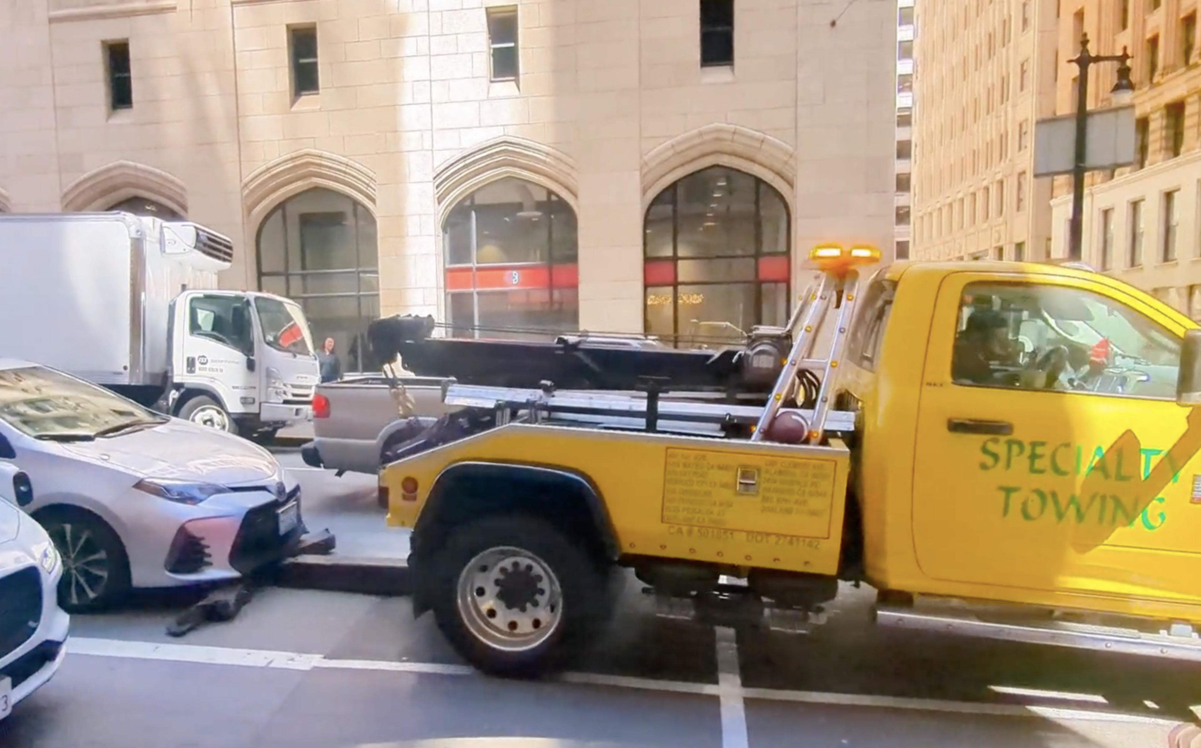 a yellow tow truck attempts to tow a silver sedan