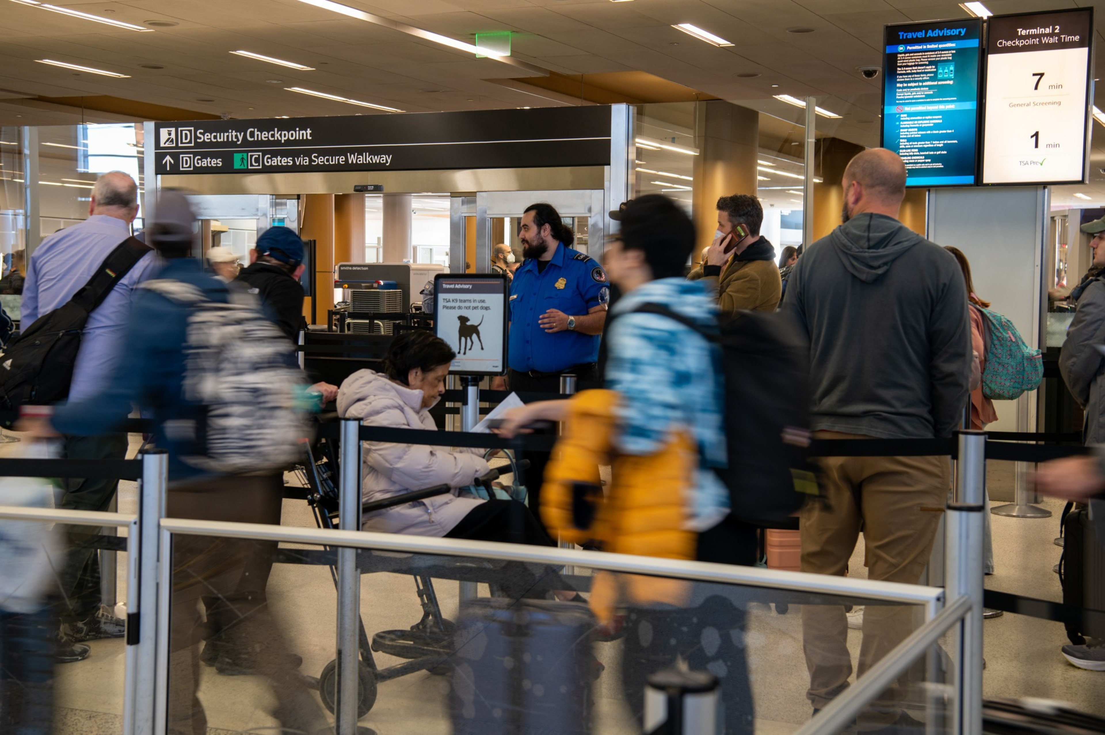 A security checkpoint as people wait in line and TSA agents checking boarding passes and id's.