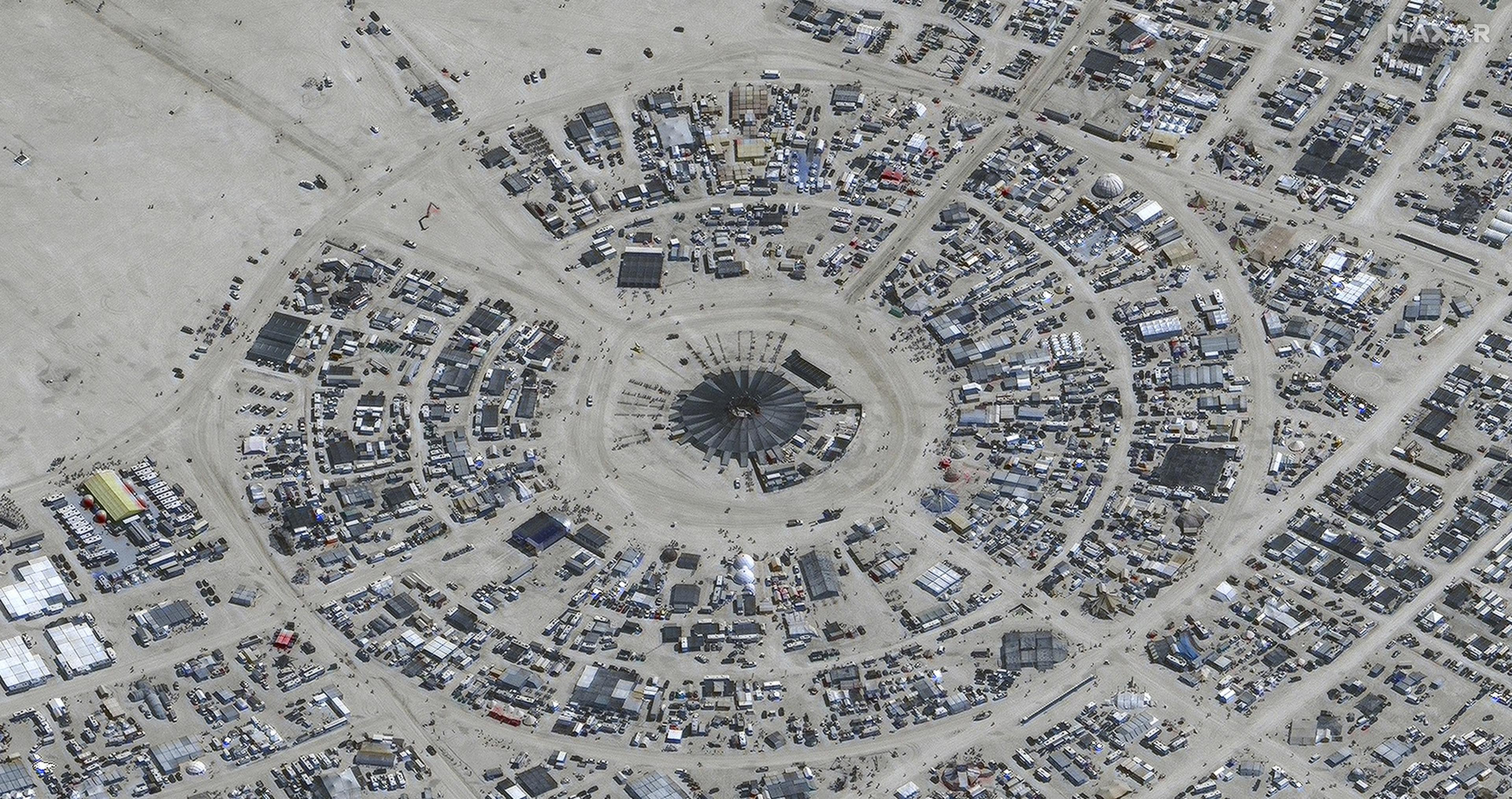 The image shows a circular encampment in a desert, with concentric roads and numerous scattered structures, resembling a temporary festival site.