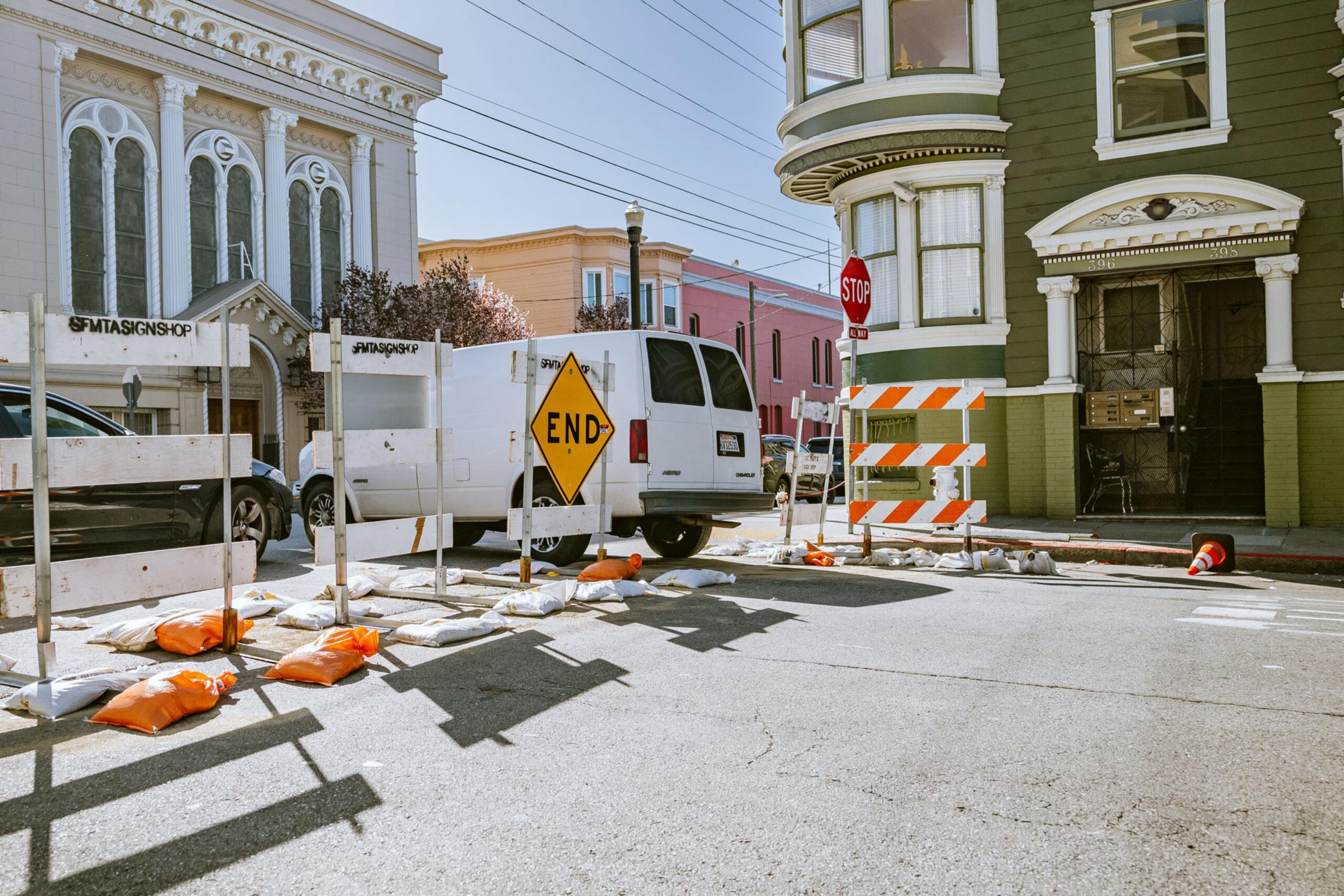Barriers block a road in San Francisco near Victorian buildings and a white van.