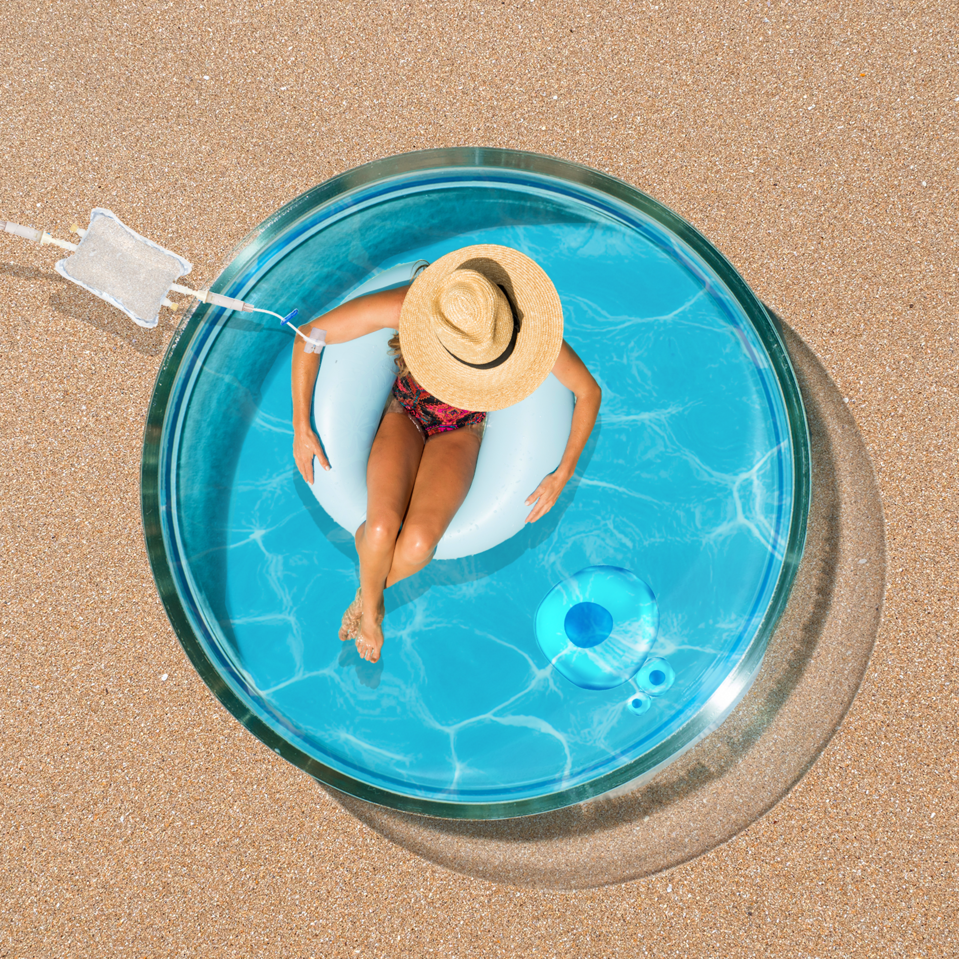 A person in a straw hat relaxes on a white float in a small, clear pool on sandy ground. Bright, sunny setting with blue water and shadows visible.