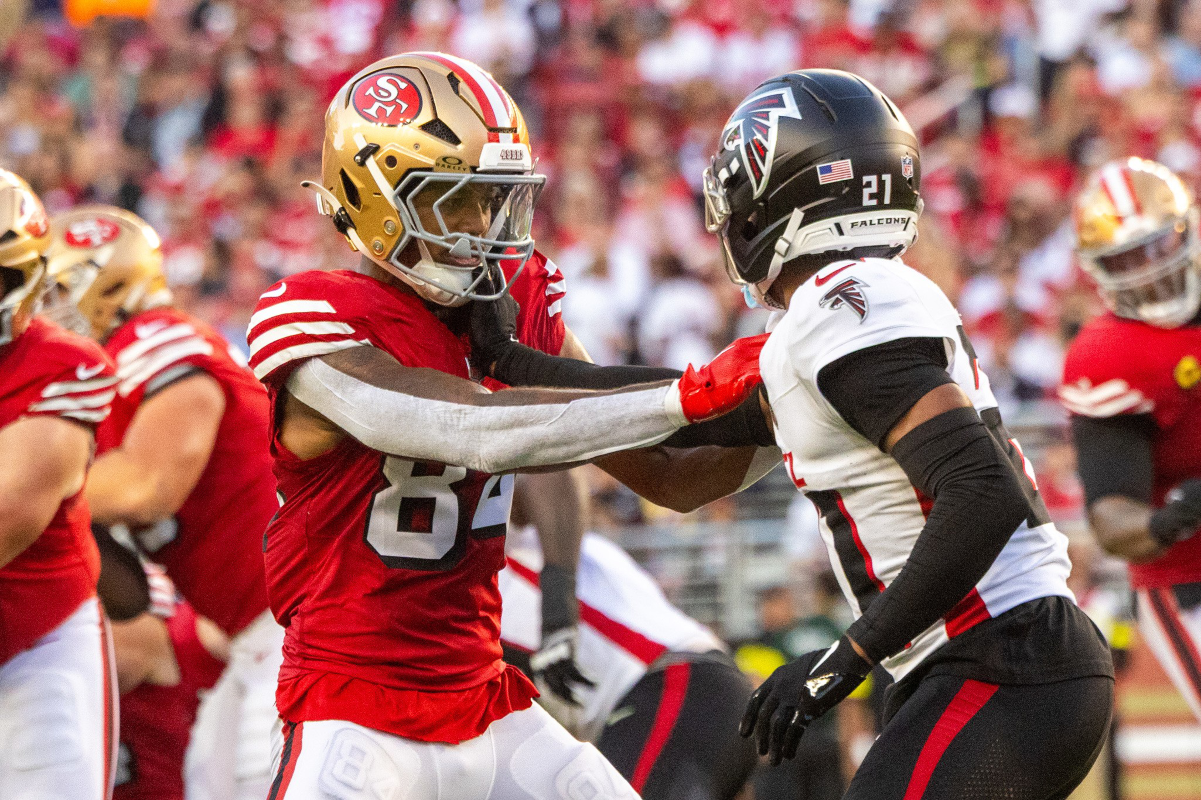 A San Francisco 49ers player in red jersey pushes against a black-jerseyed Atlanta Falcons player during a football game.