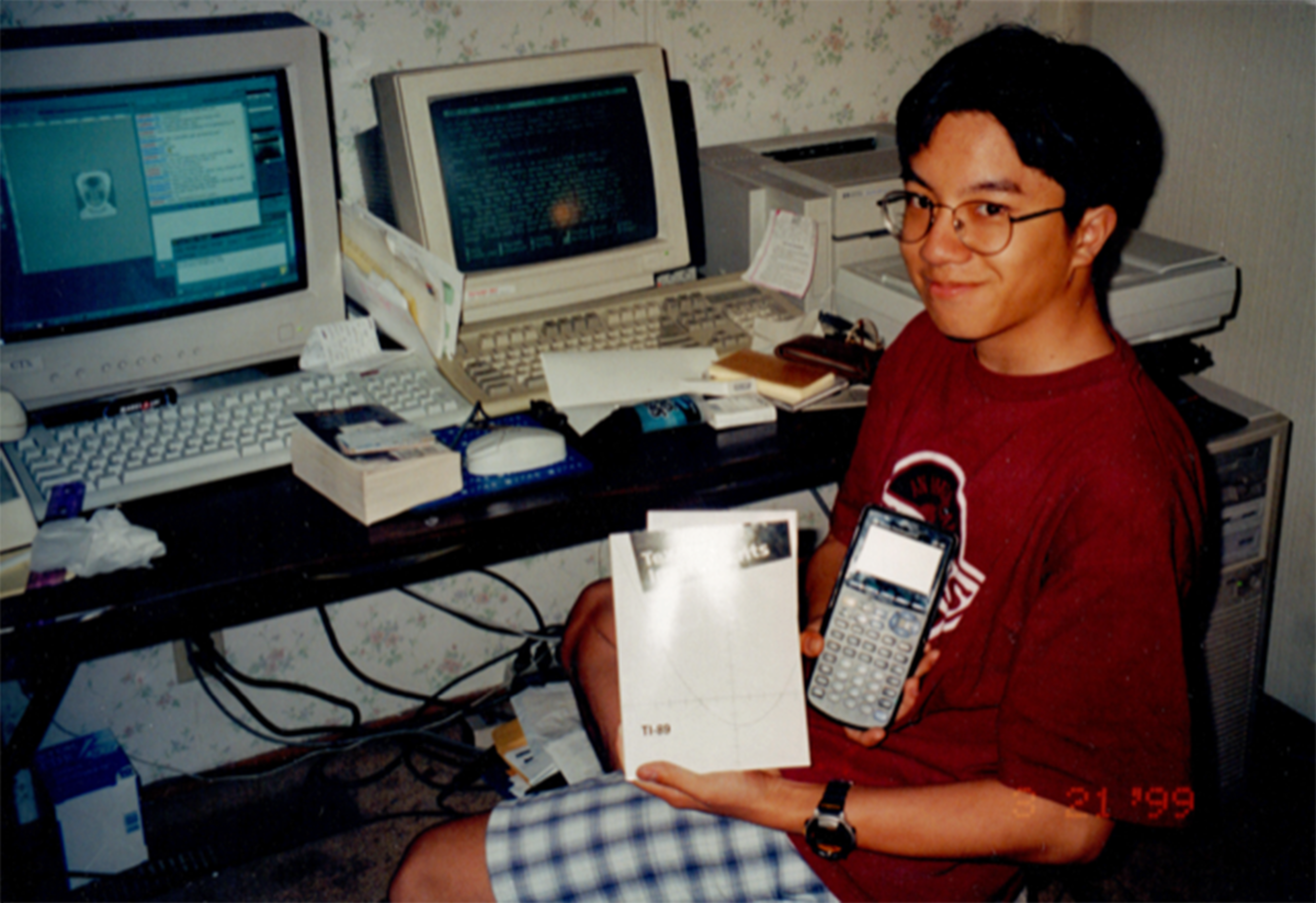 A young person with glasses sits cross-legged holding a TI-89 calculator and its manual, with two old computer monitors on a desk behind them.