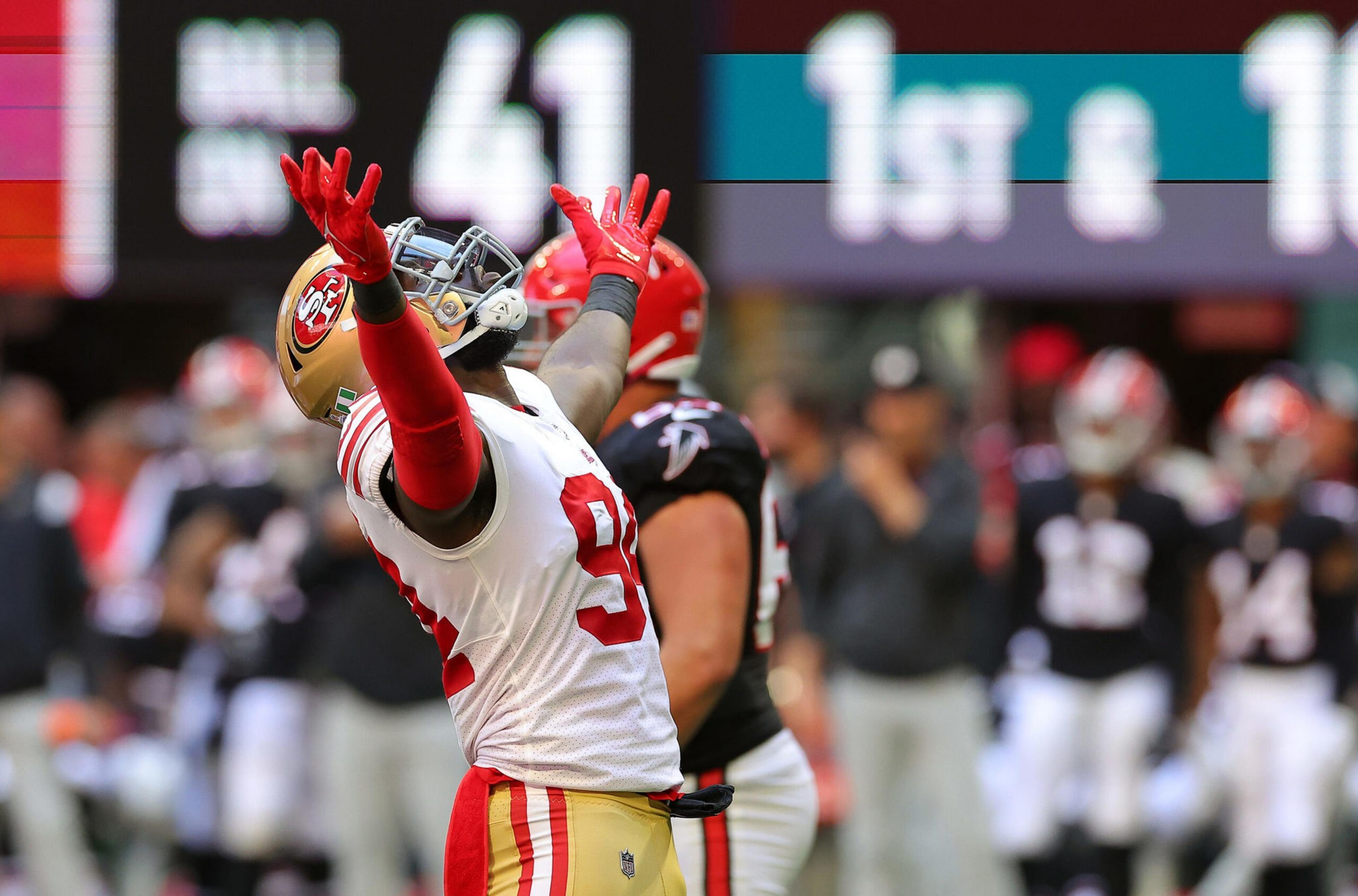 A football player in a San Francisco 49ers uniform celebrates with arms raised, while a player in a black Atlanta Falcons uniform stands nearby.