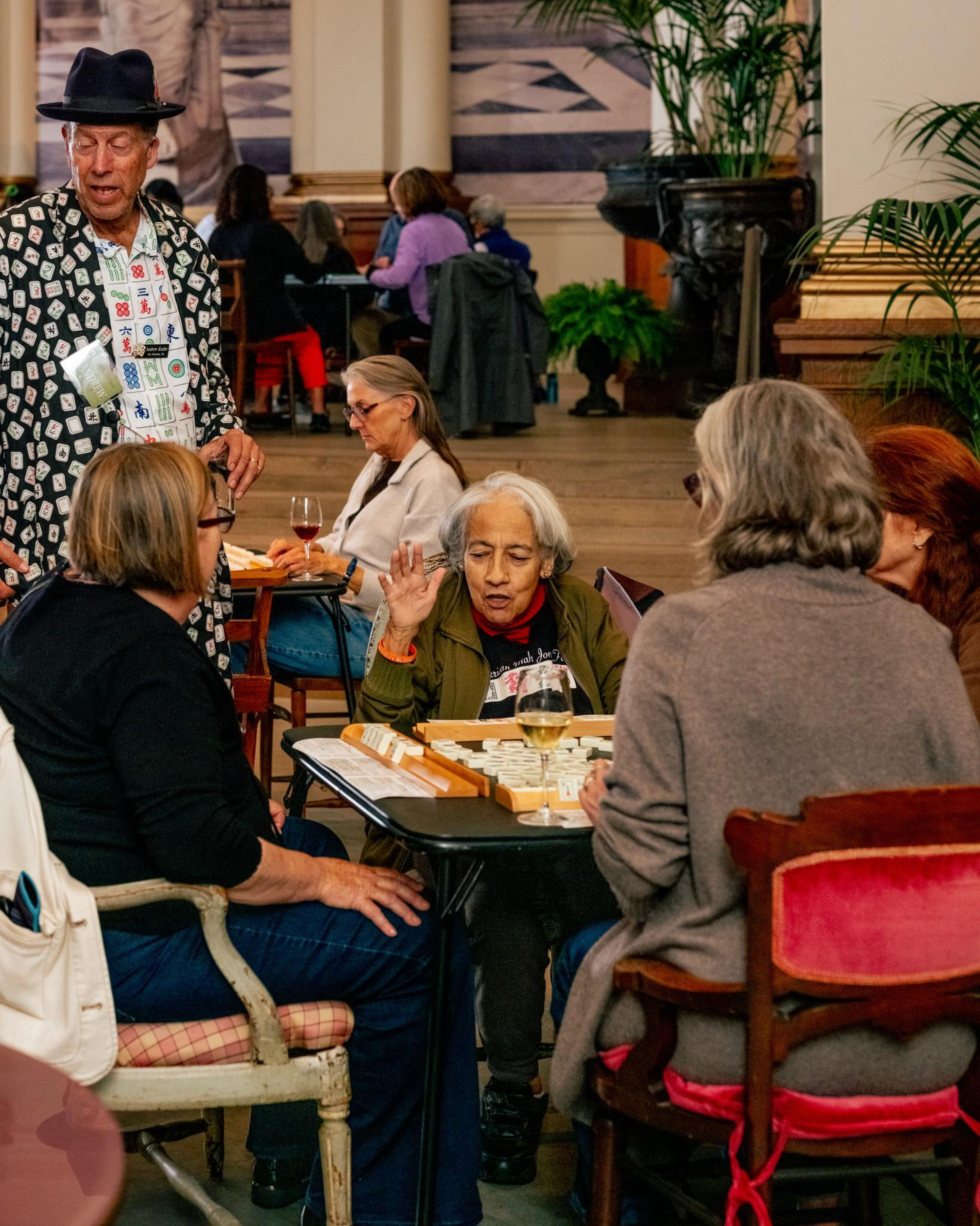 Several adults sit around a table, engaged in a group activity or discussion, with papers and drinks in front of them in a cozy indoor setting.