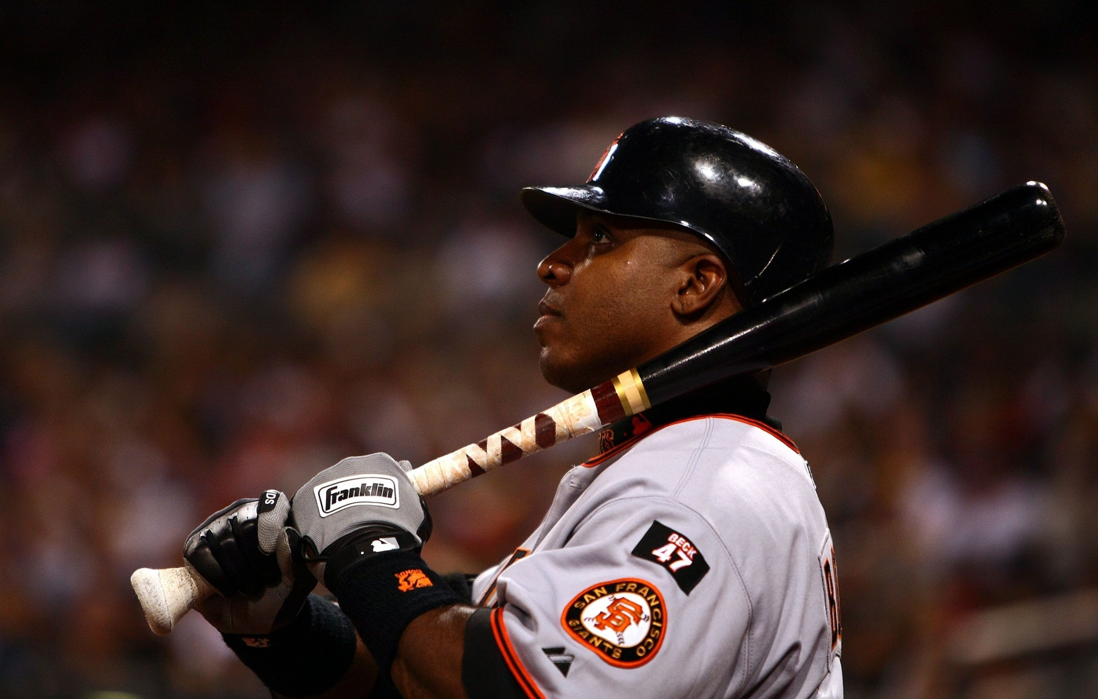 A baseball player wearing a San Francisco Giants uniform and helmet holds a bat over his shoulder, looking intently forward.