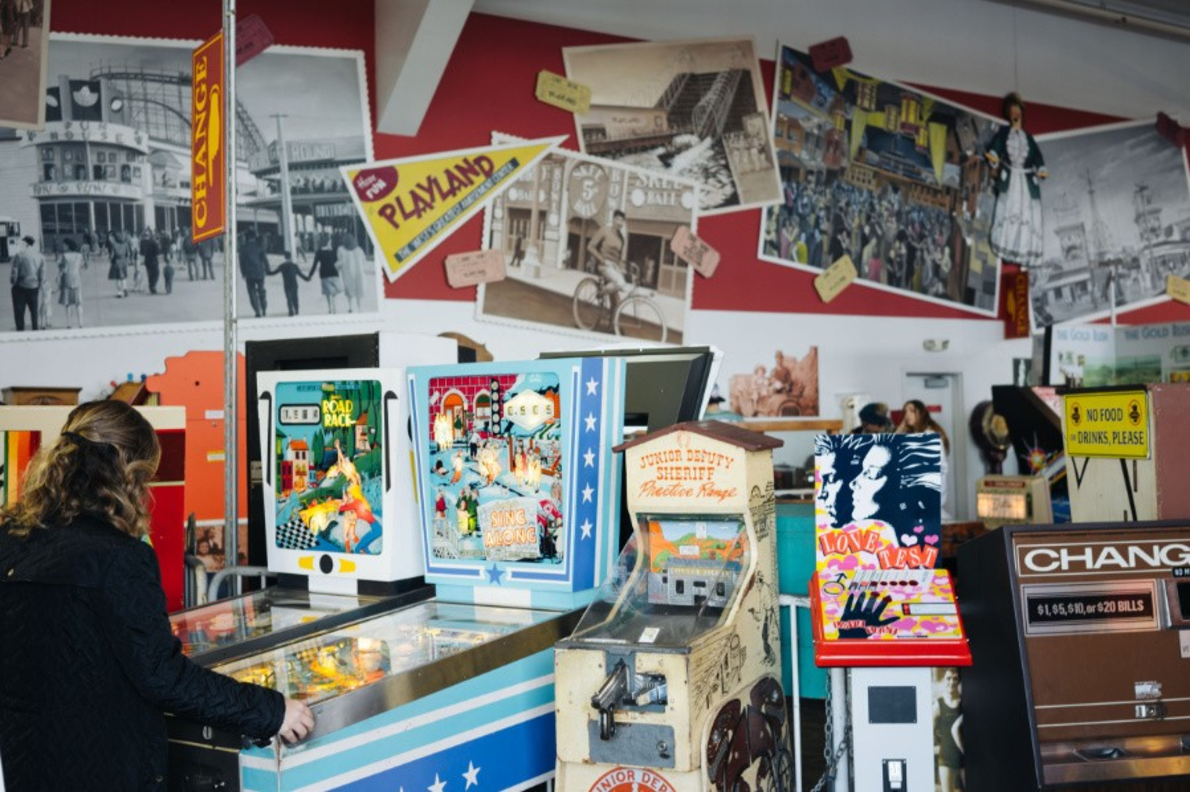 A person plays a classic pinball game against a wall filled with old posters. 