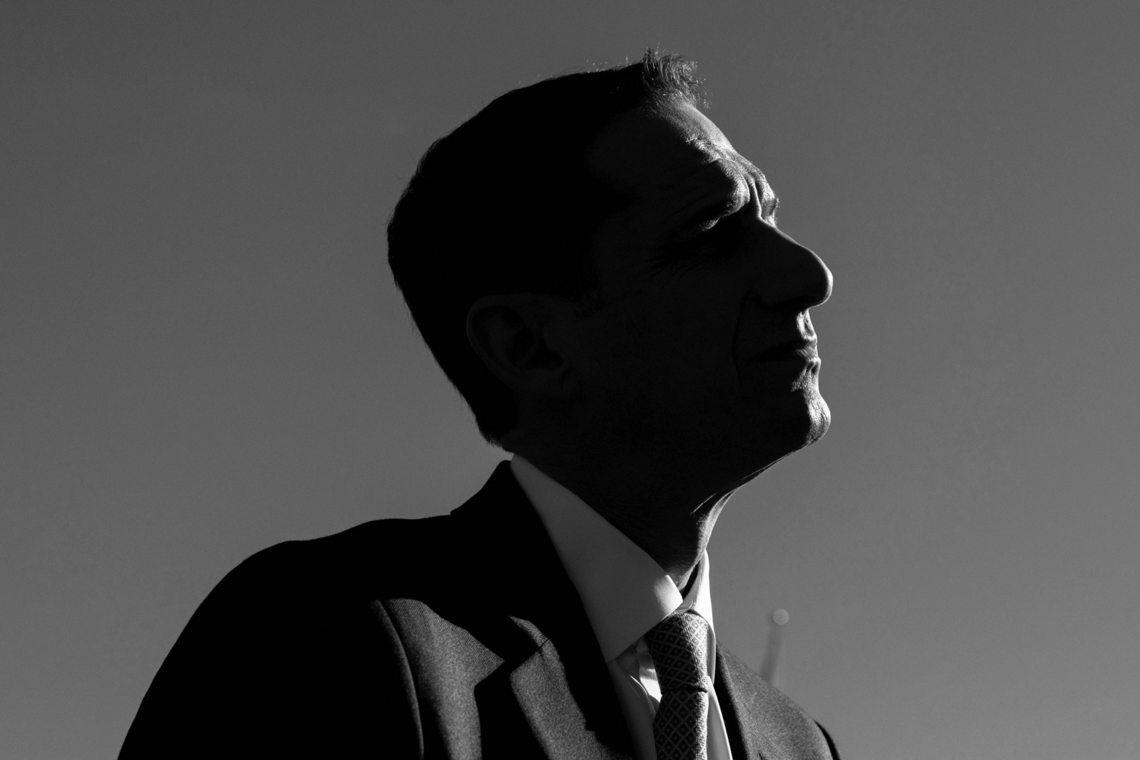 A silhouette of a man in a suit and tie is shown against a plain background, his face in profile, looking upward with distinct shadows highlighting his features.