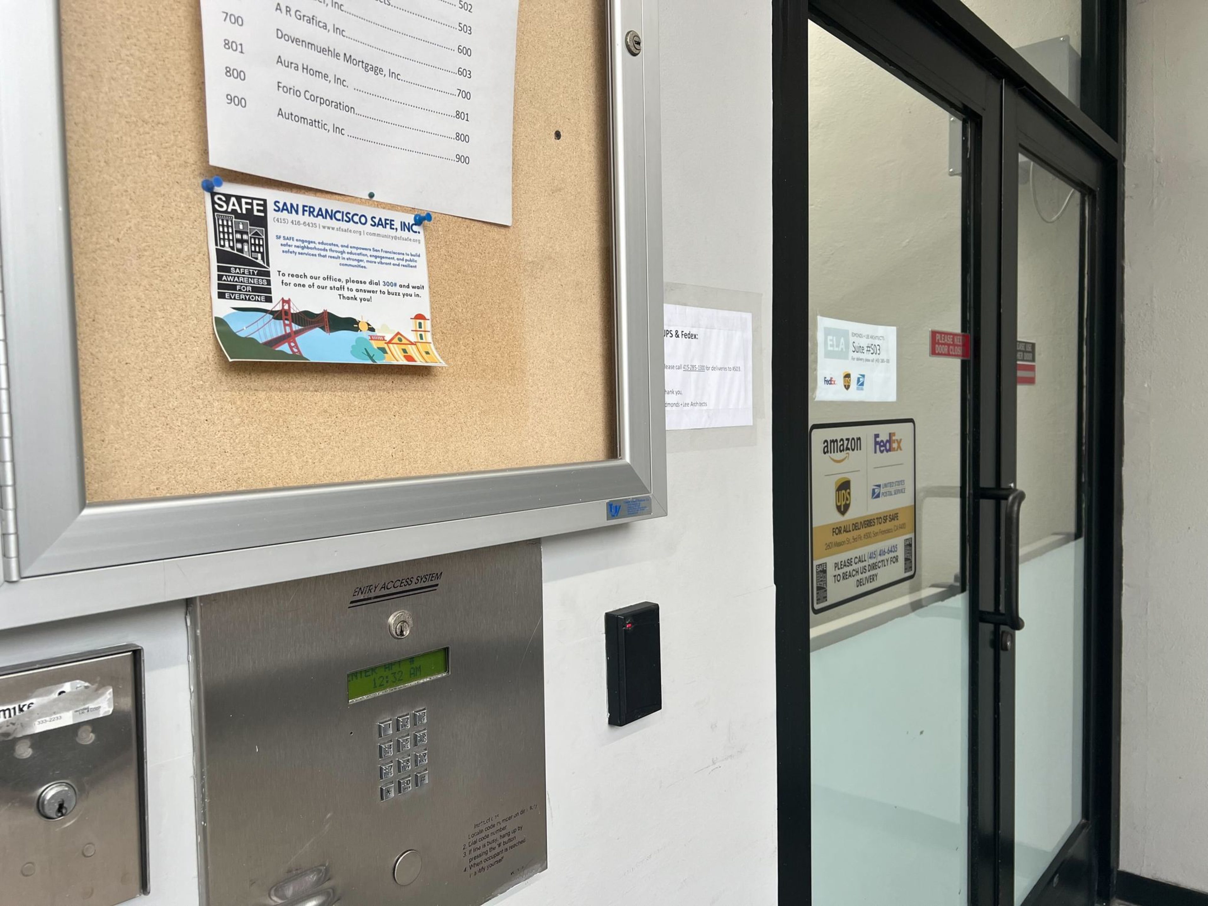An entry to a building with glass doors and bulletin board. 
