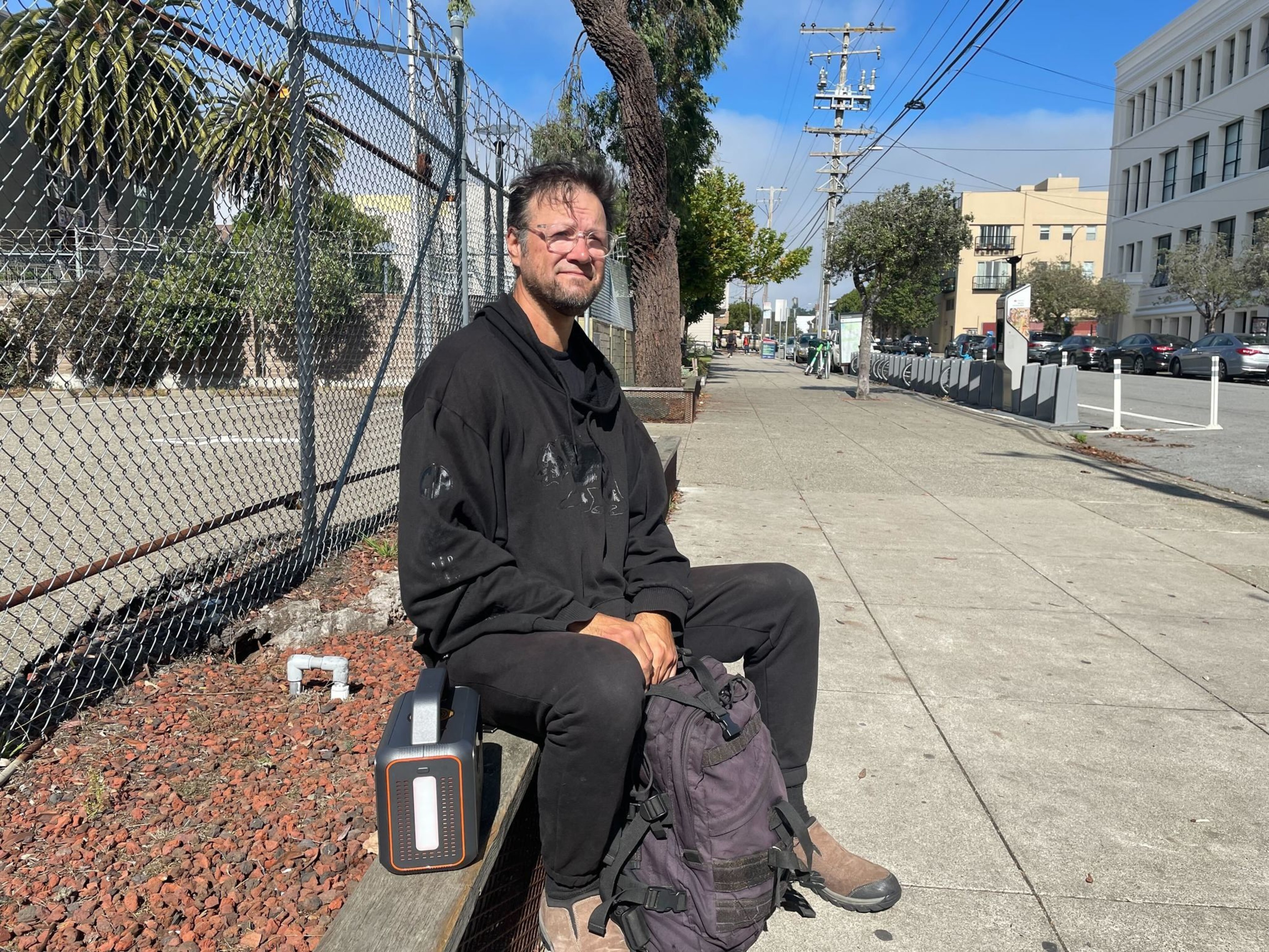 A man sits near the sidewalk.