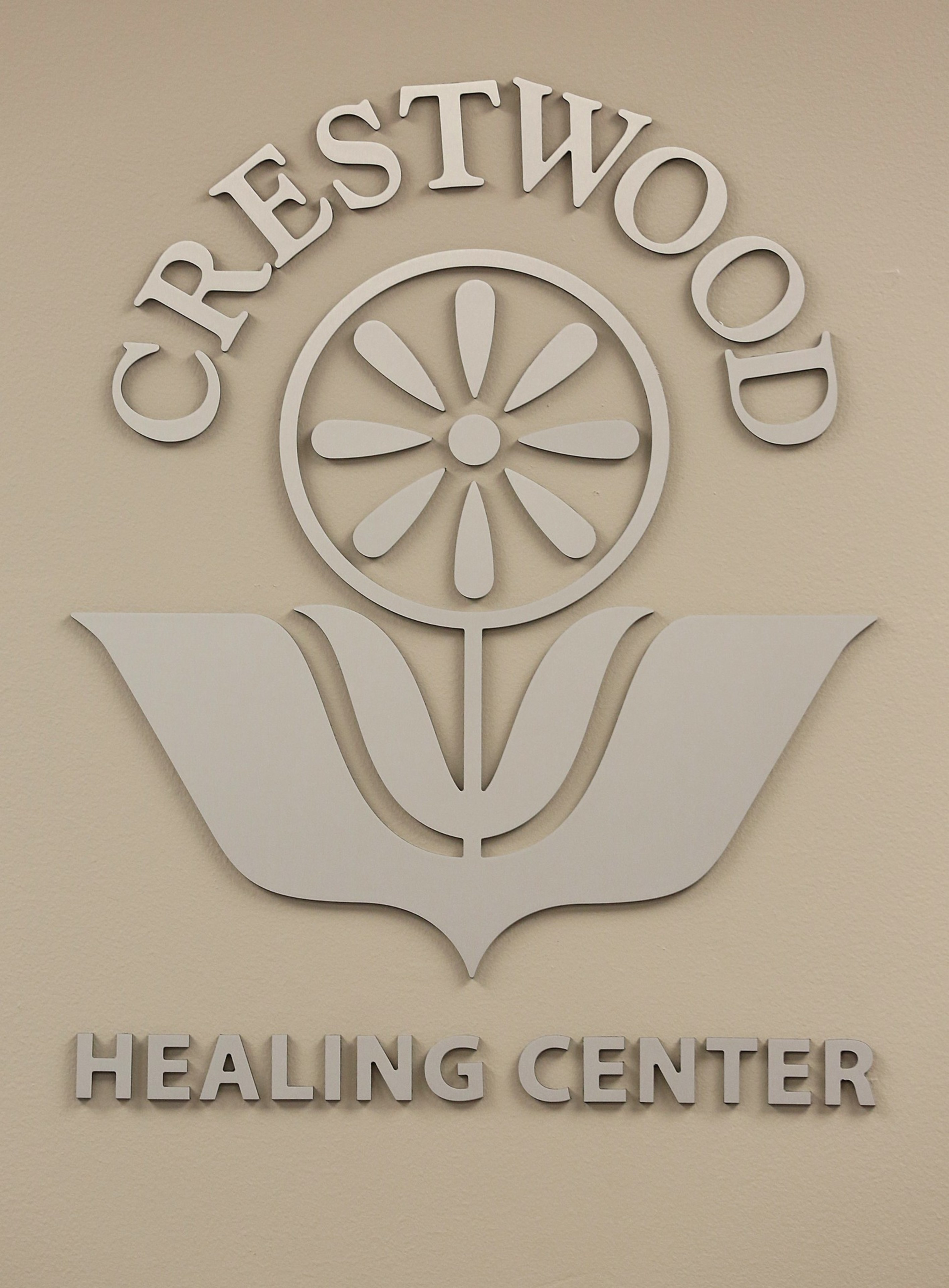 The words “CRESTWOOD HEALING CENTER” surround a stylized flower emblem with petals inside a circle and two large leaves below.