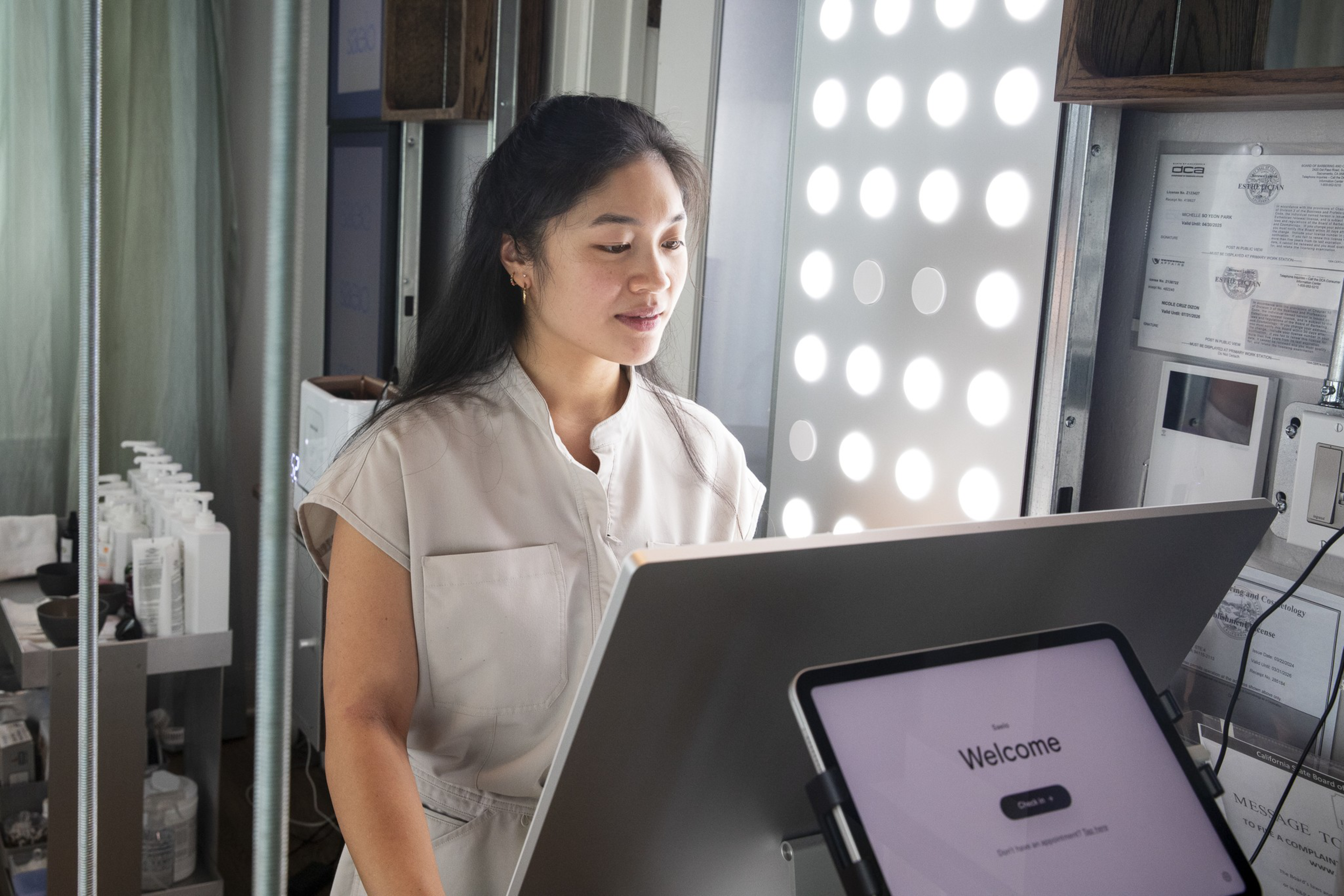 A woman stands at a counter with a welcome screen on a tablet in front of her and circular lights illuminating the background.