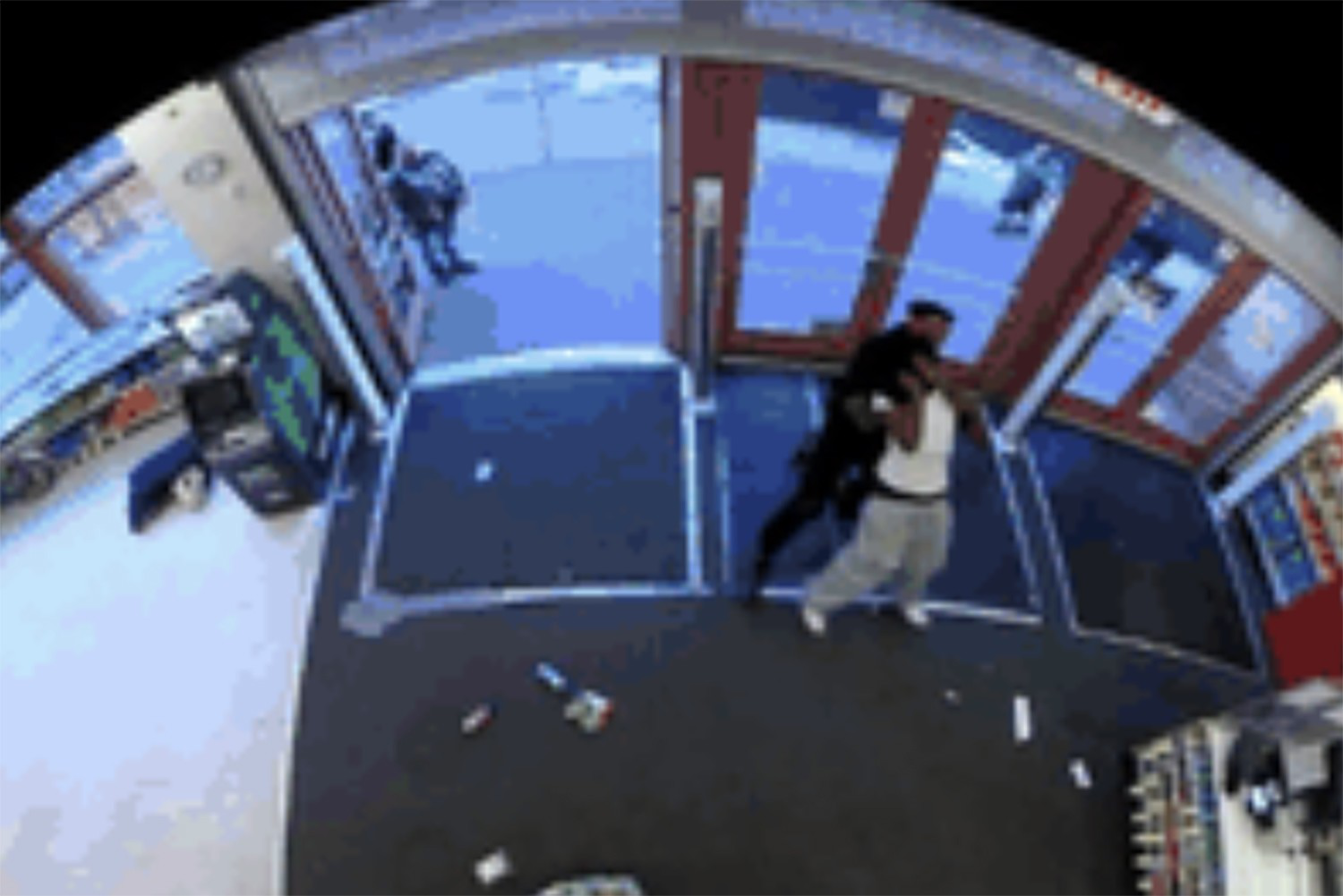 A security camera captures two people near a store entrance, with one person holding the other from behind against the glass doors.