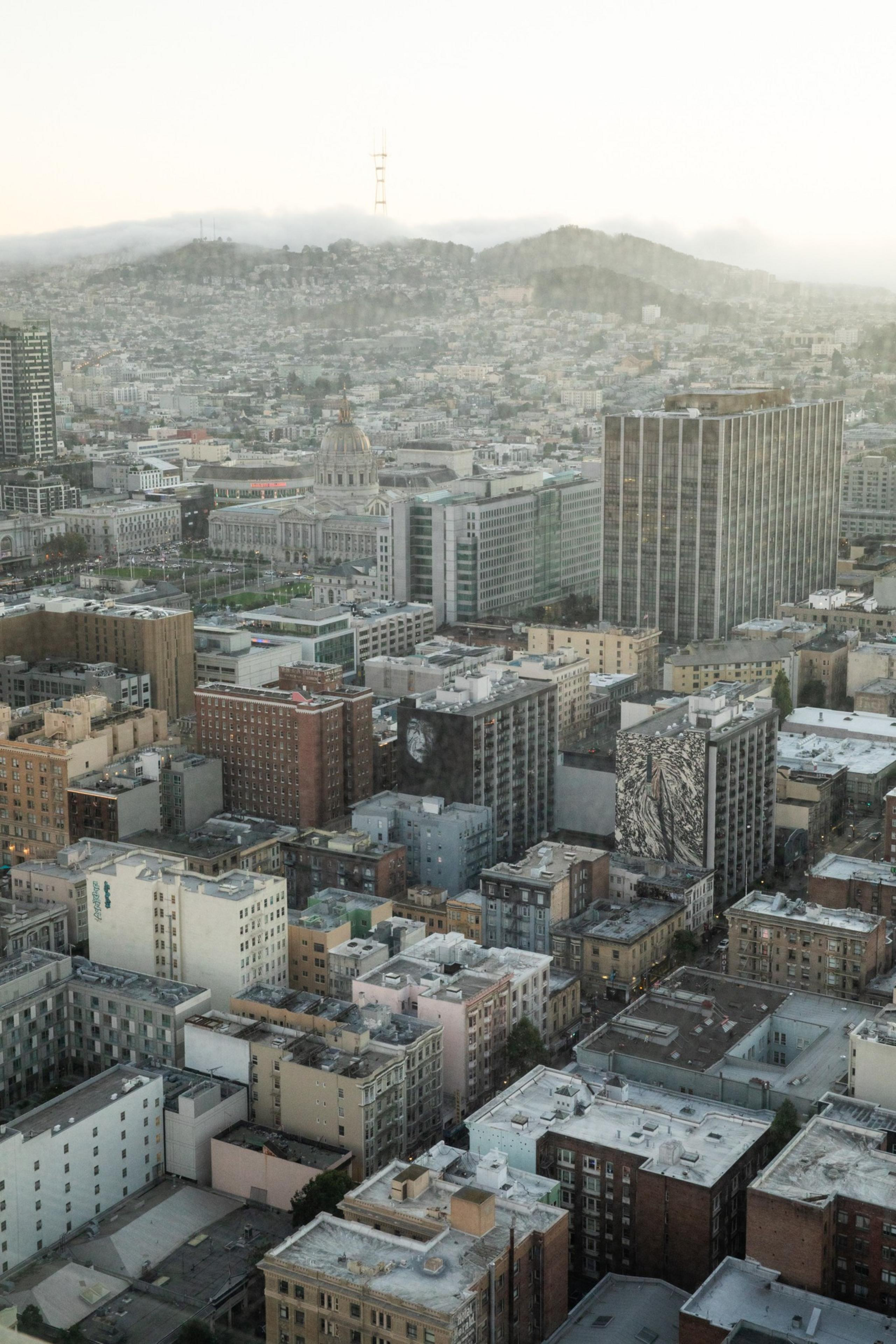 The image shows a cityscape with numerous buildings, including a prominent domed structure and a tall tower on a distant, fog-covered hill. The scene is viewed from above.