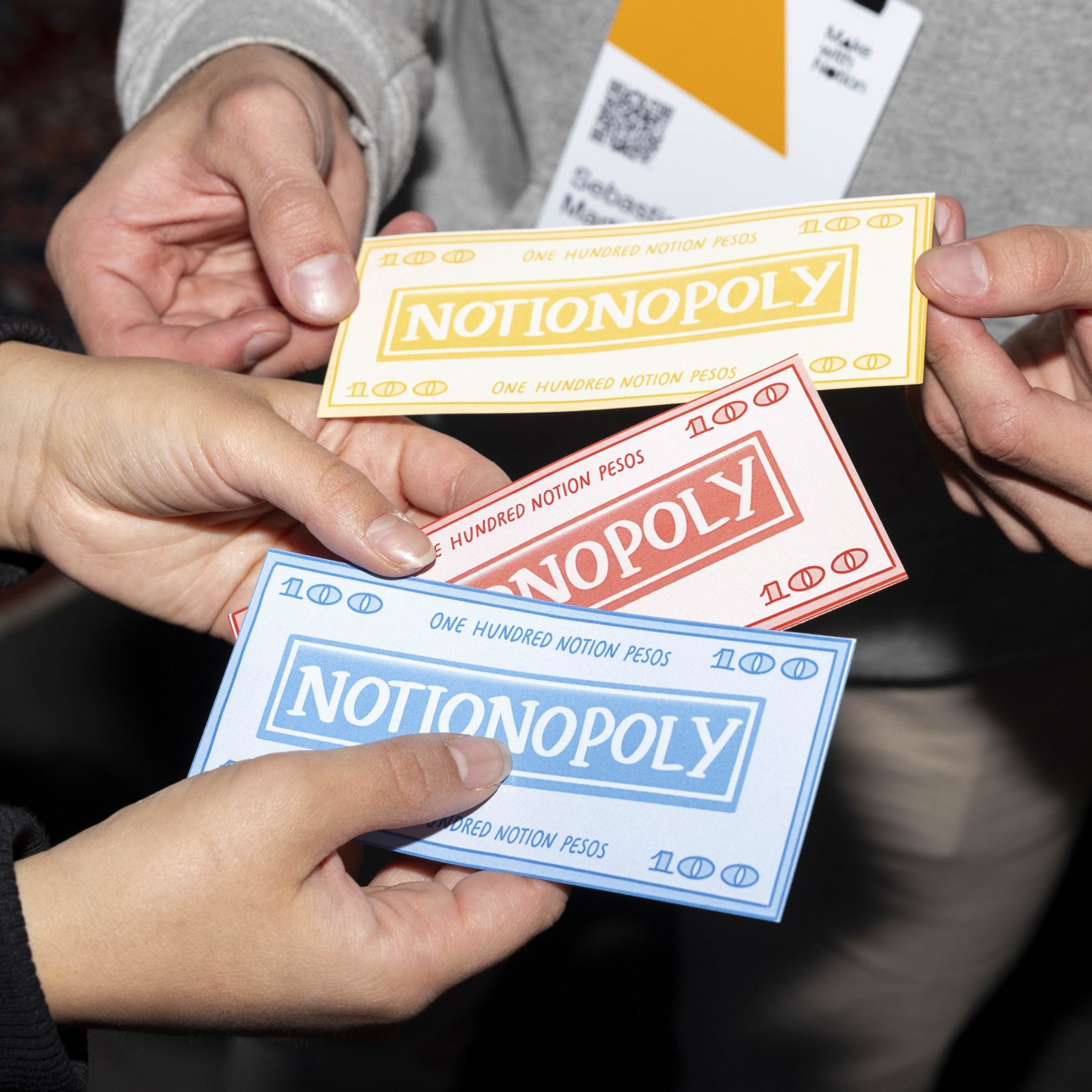 Three people hold colorful play money labeled &quot;Notionopoly&quot; in yellow, red, and blue, each worth one hundred &quot;Notion Pesos.&quot;