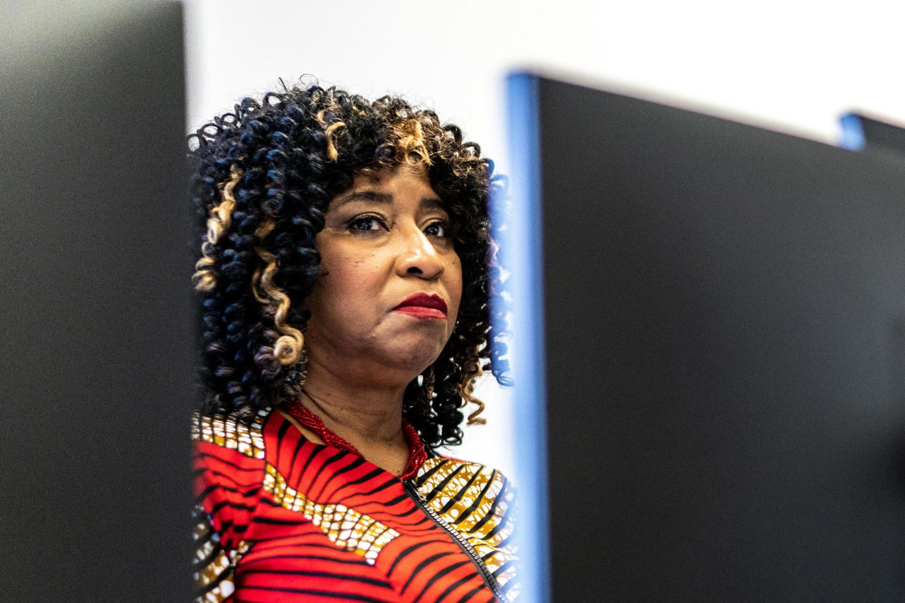 A woman looks at the camera from behind a computer monitor.