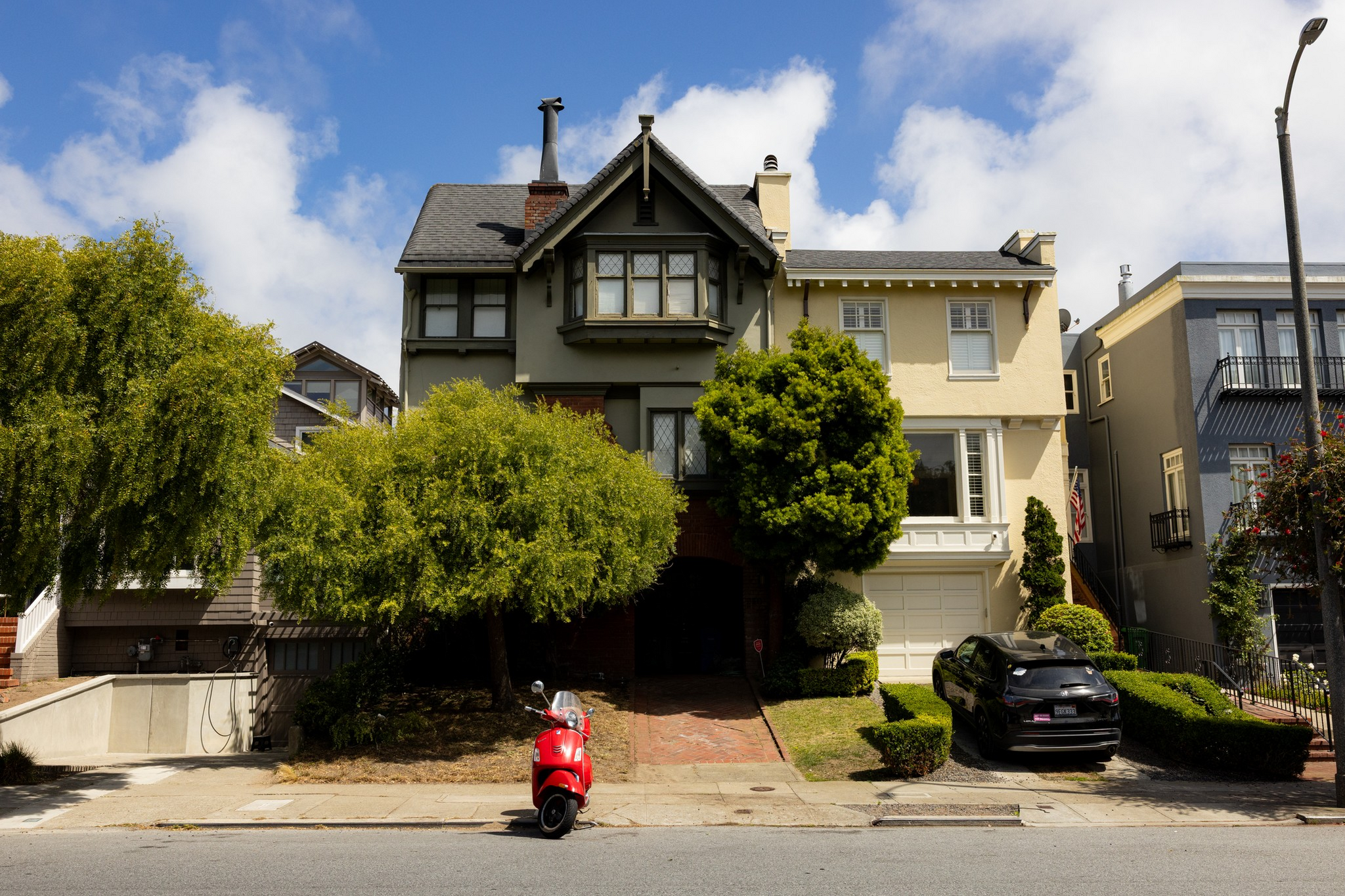 Two attached houses with distinct colors—one grey and one cream—stand side by side, with trees and a red scooter parked on the street.