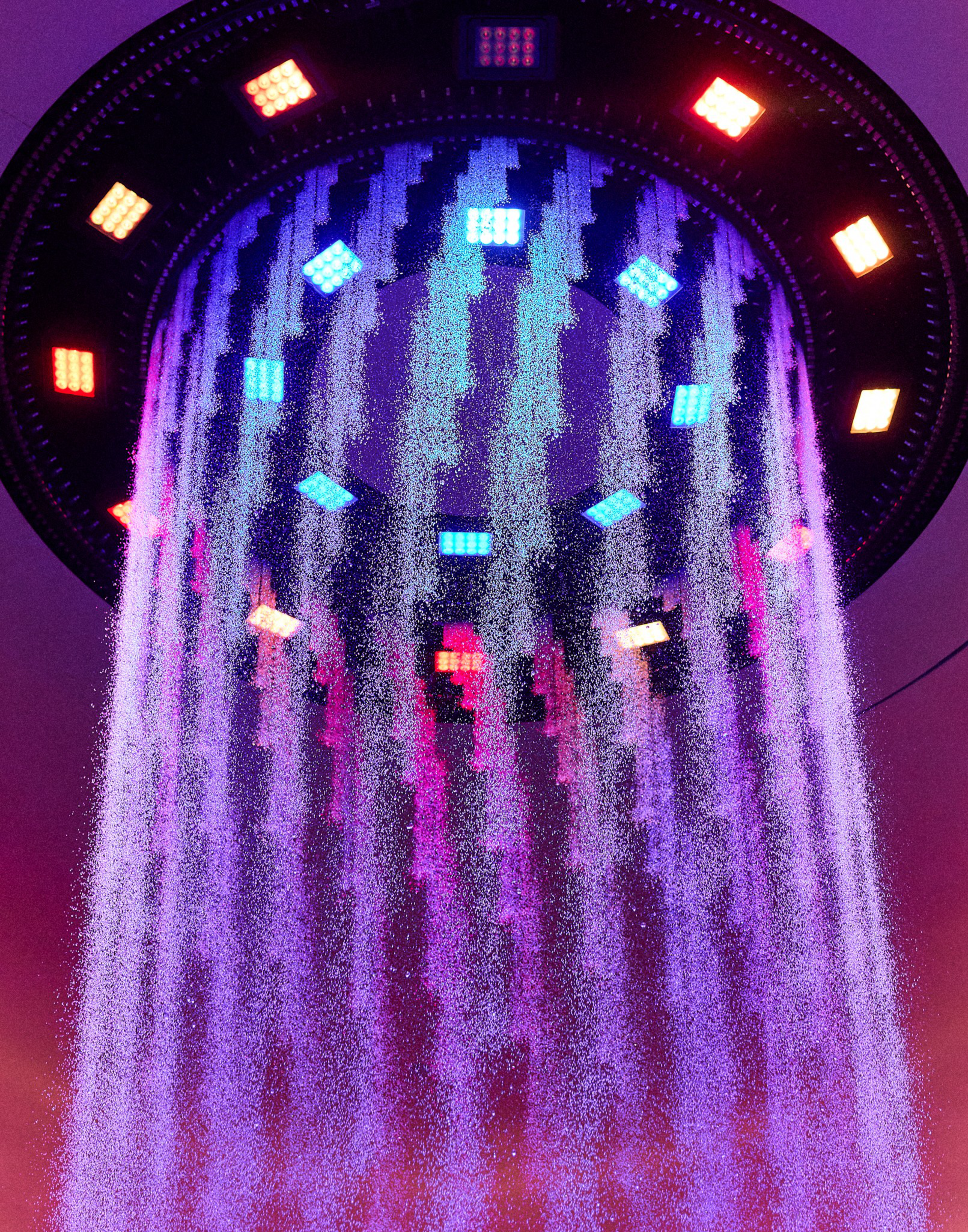 A circular showerhead emits glowing purple-lit water streams with colorful red, blue, and yellow LED lights around its rim and inside.
