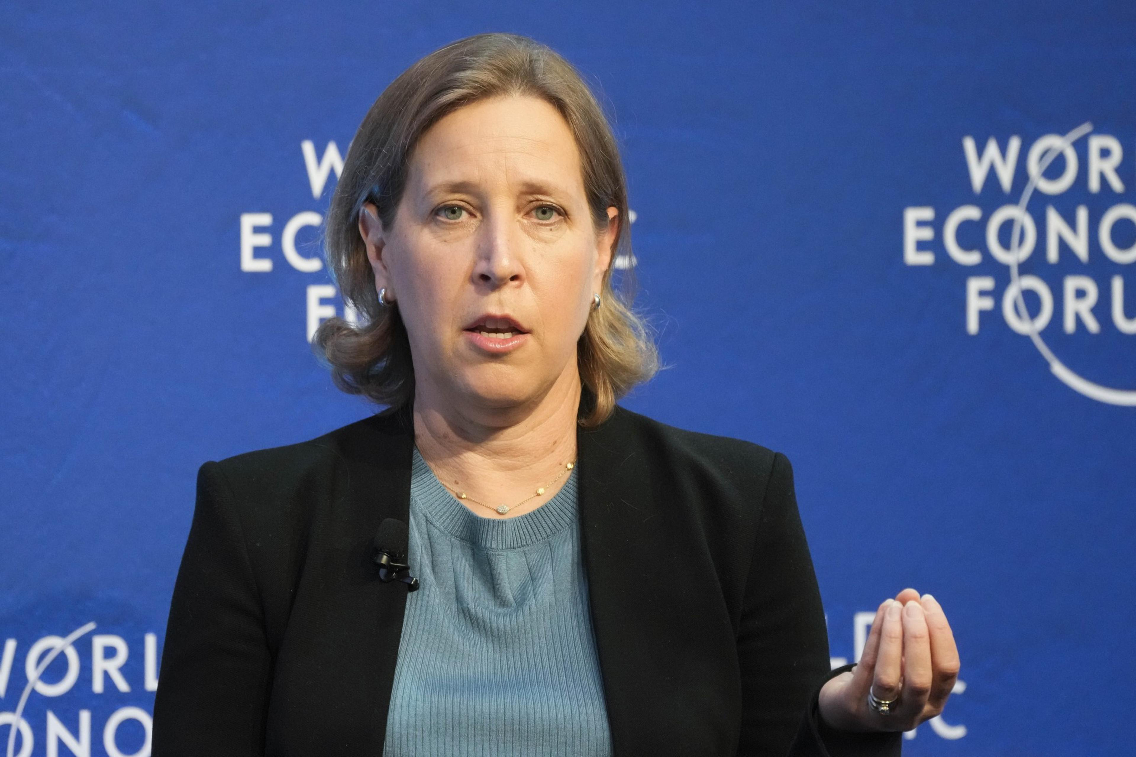 A woman with light brown hair speaks, raising one hand slightly. She is wearing a black blazer over a blue top. The background displays "World Economic Forum."