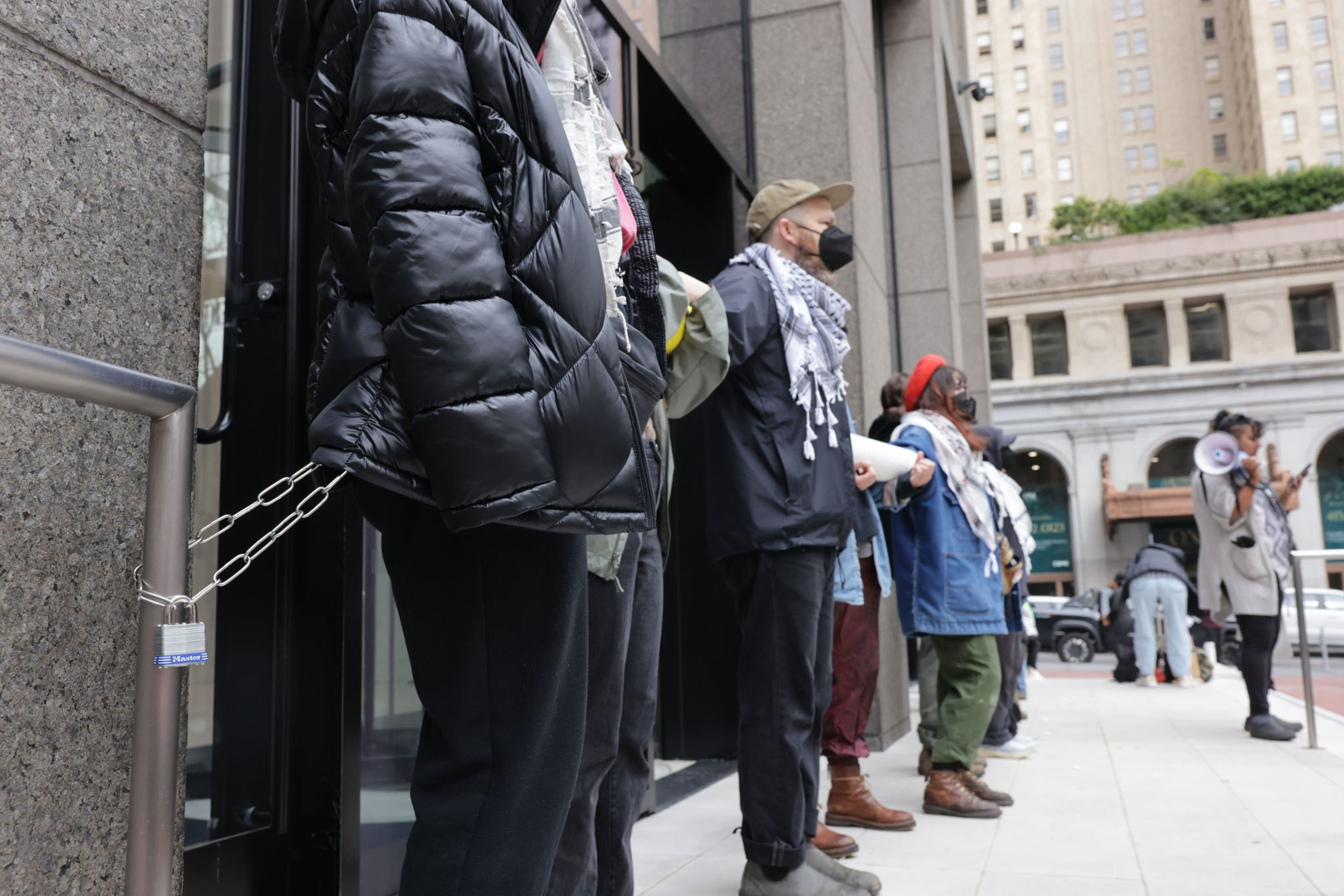 Chains connect several people in dark clothing lined up outside the entrance of a building.