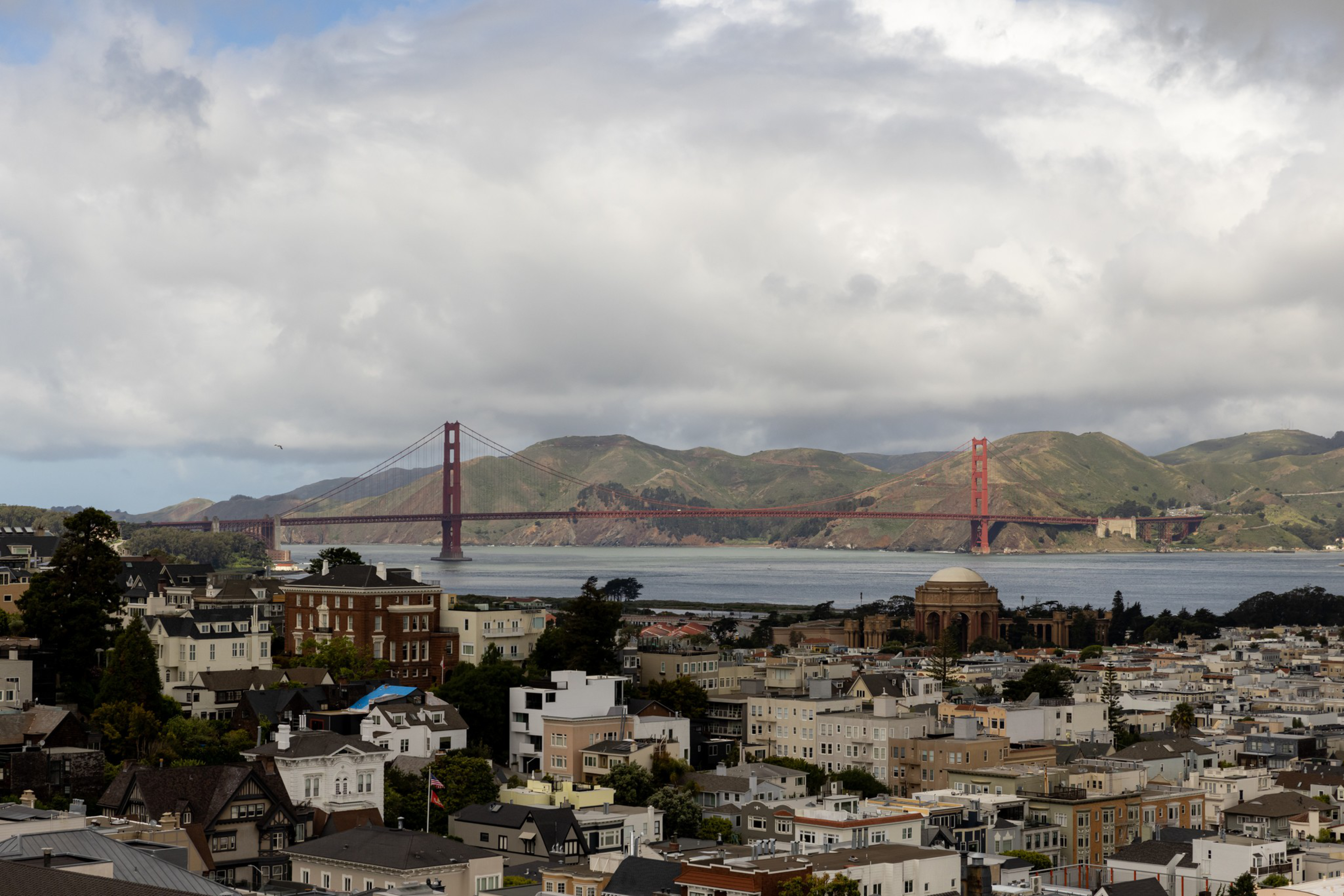 A cityscape of San Francisco features the Golden Gate Bridge spanning across the bay with hills in the background and residential buildings in the foreground.