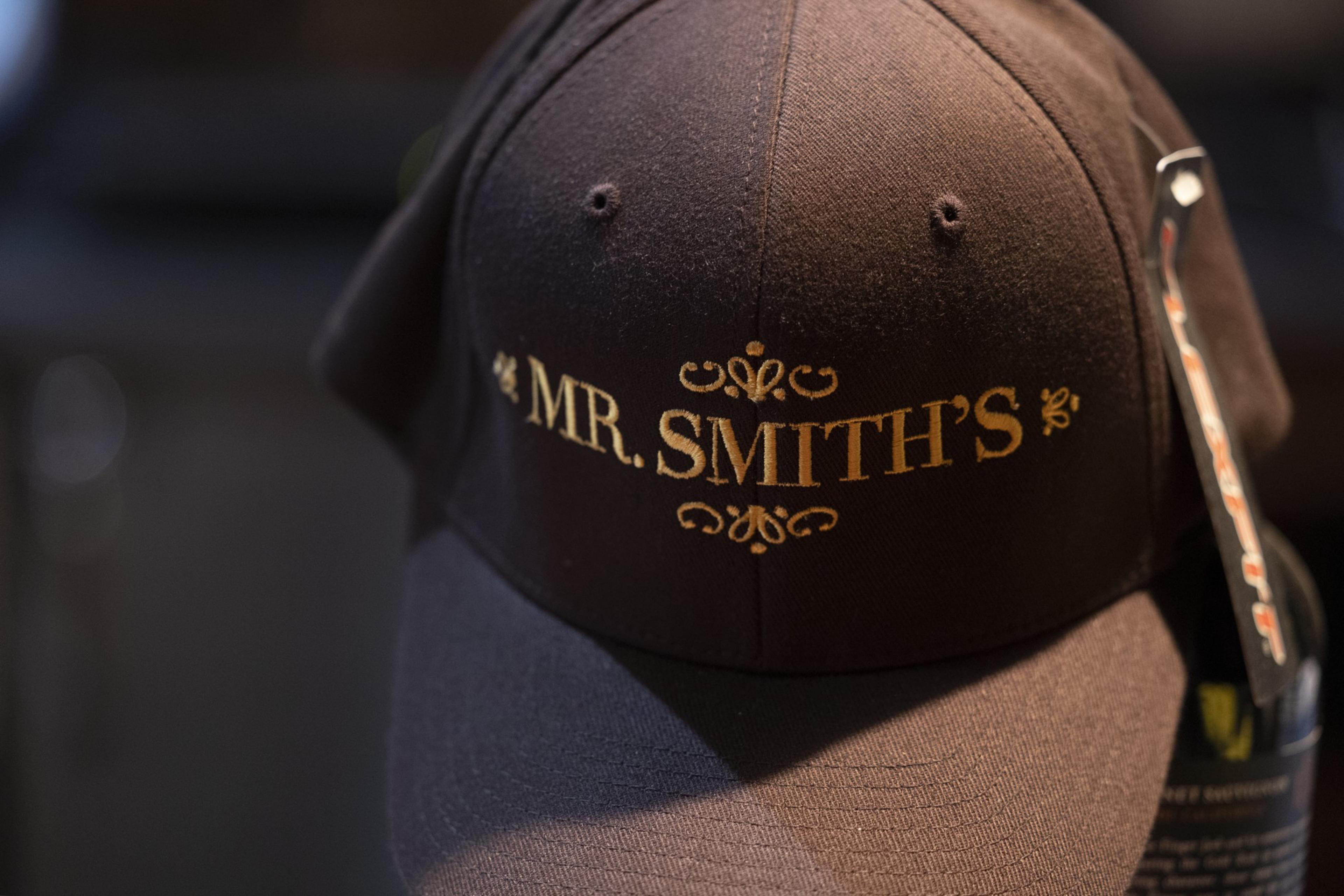 The image shows a dark brown baseball cap with the words &quot;MR. SMITH'S&quot; embroidered in gold lettering on the front.