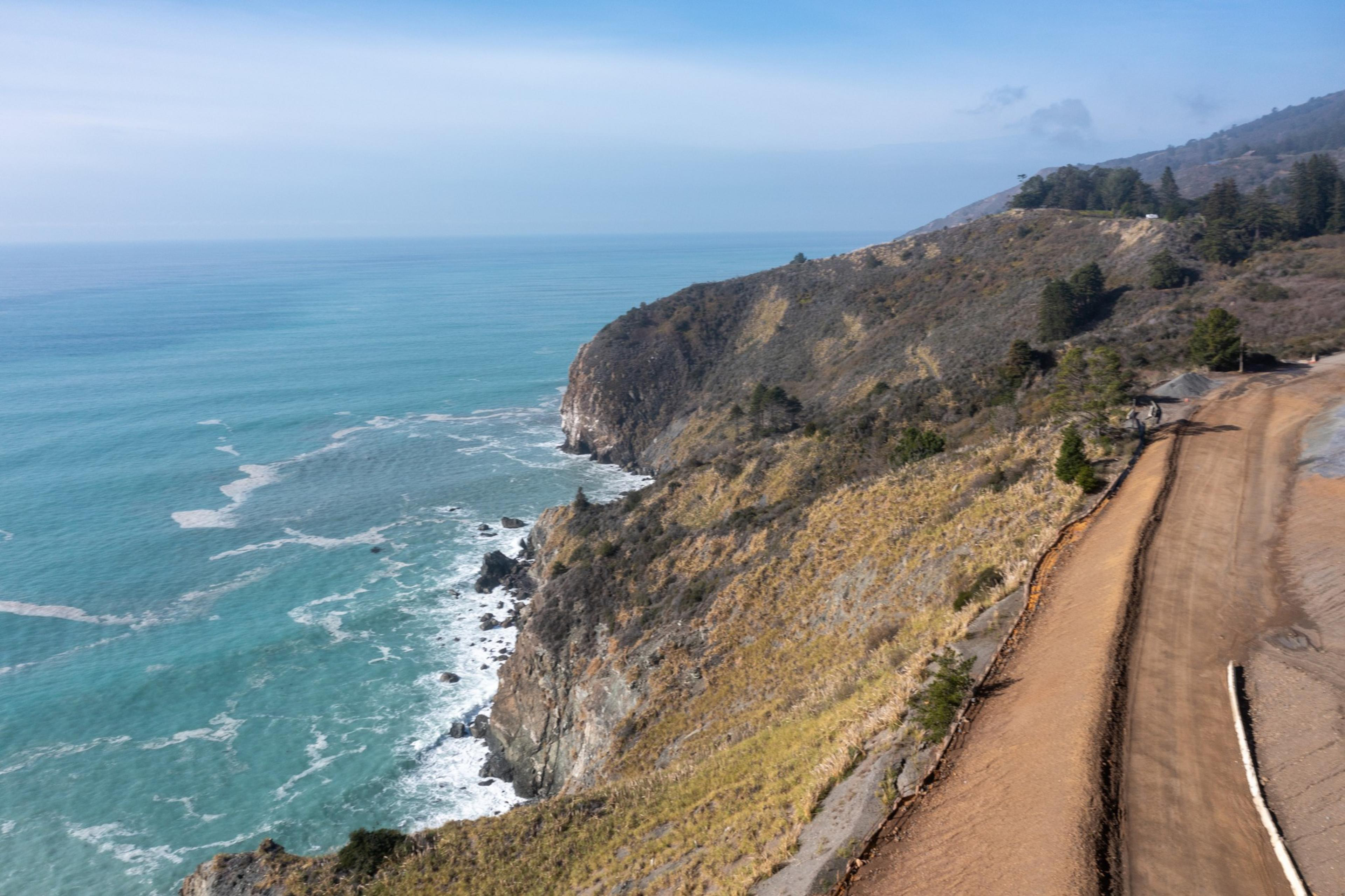 The Pacific Ocean to the left and a mountains terrain with unfinished road on the right.