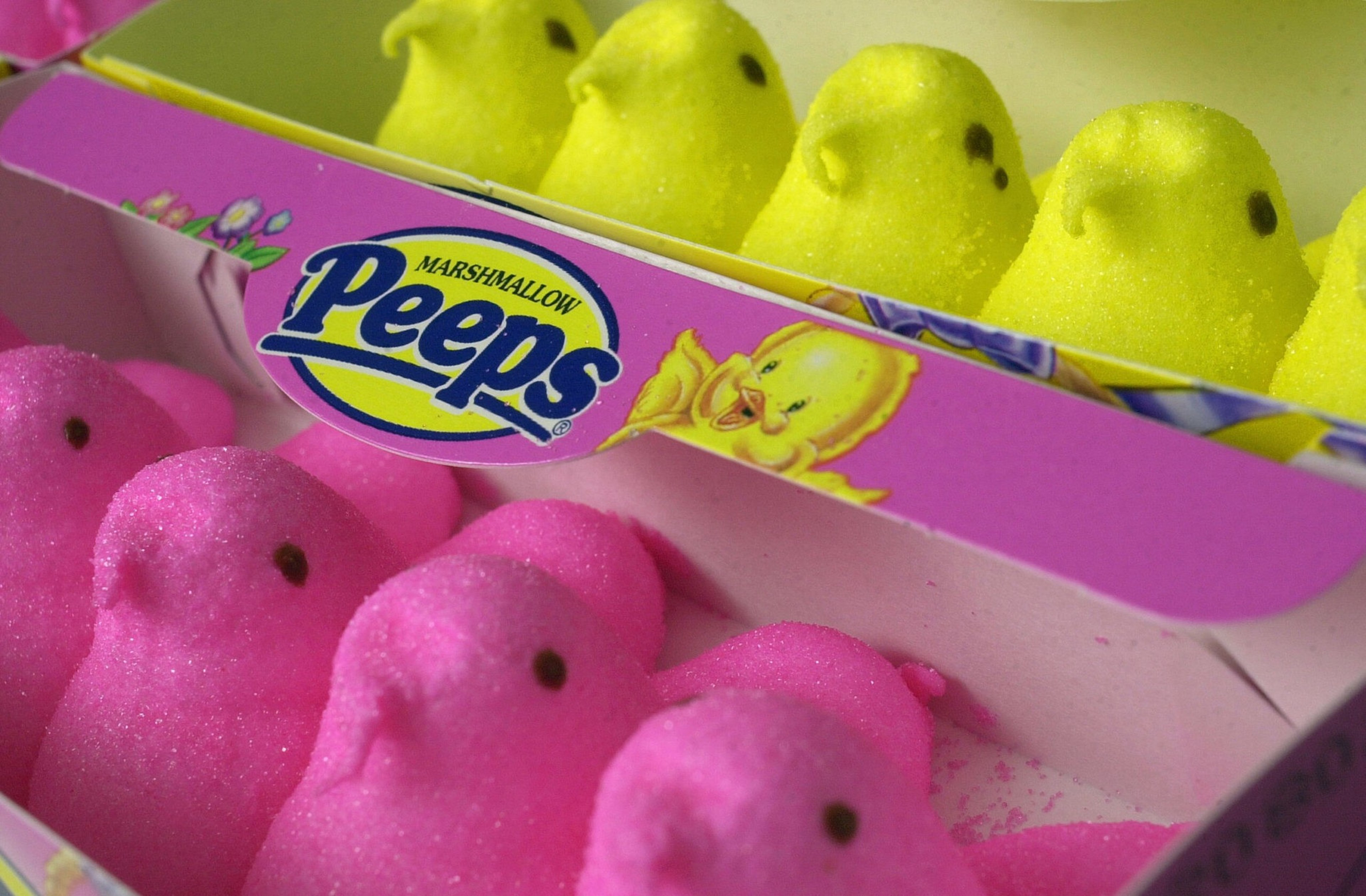 Pink and yellow marshmallow Peeps shaped like chicks are lined up in a partially open pastel purple box.