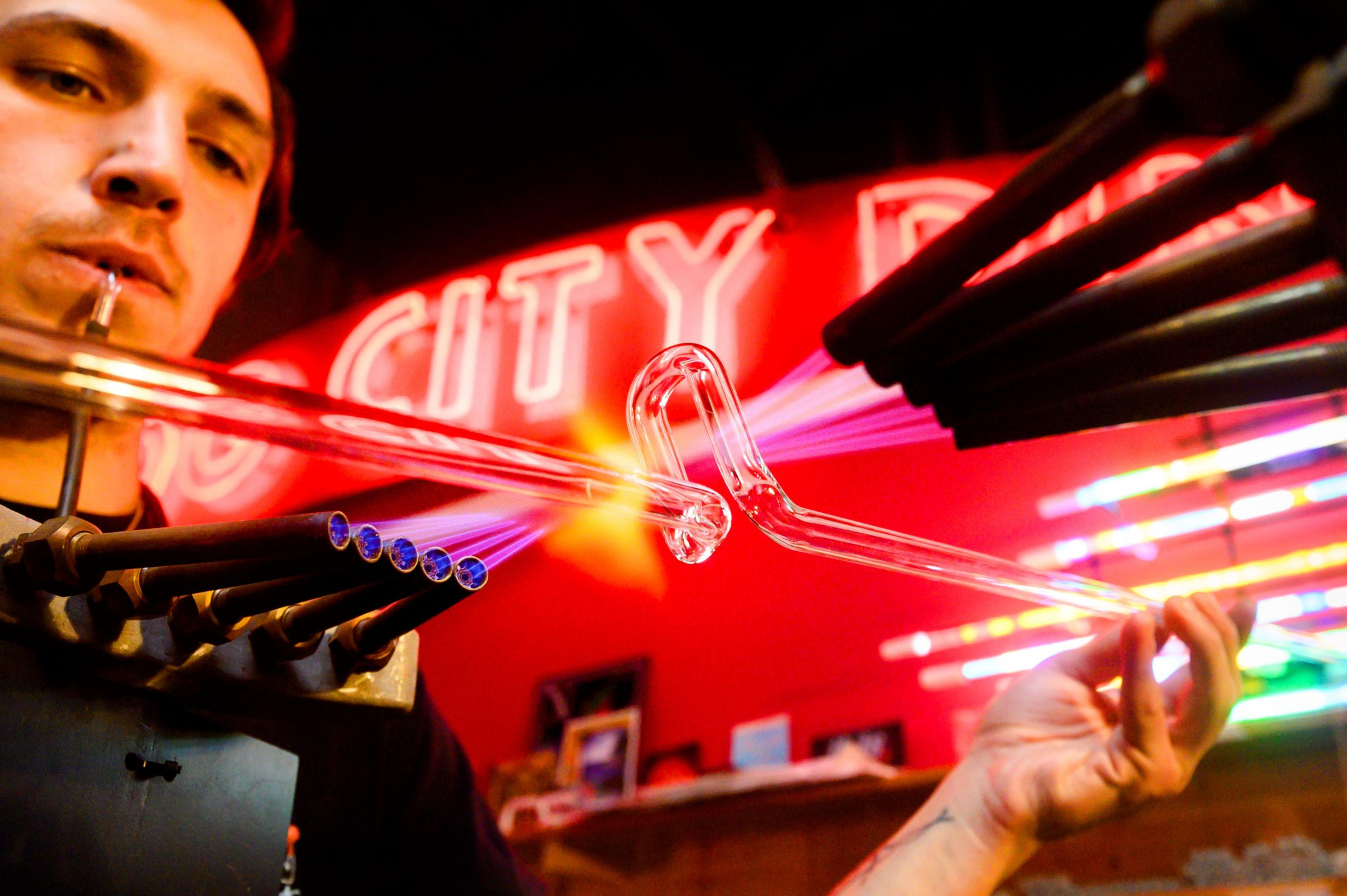 A man bends glass for a sign restoration with high heat fire coming out of tubes.