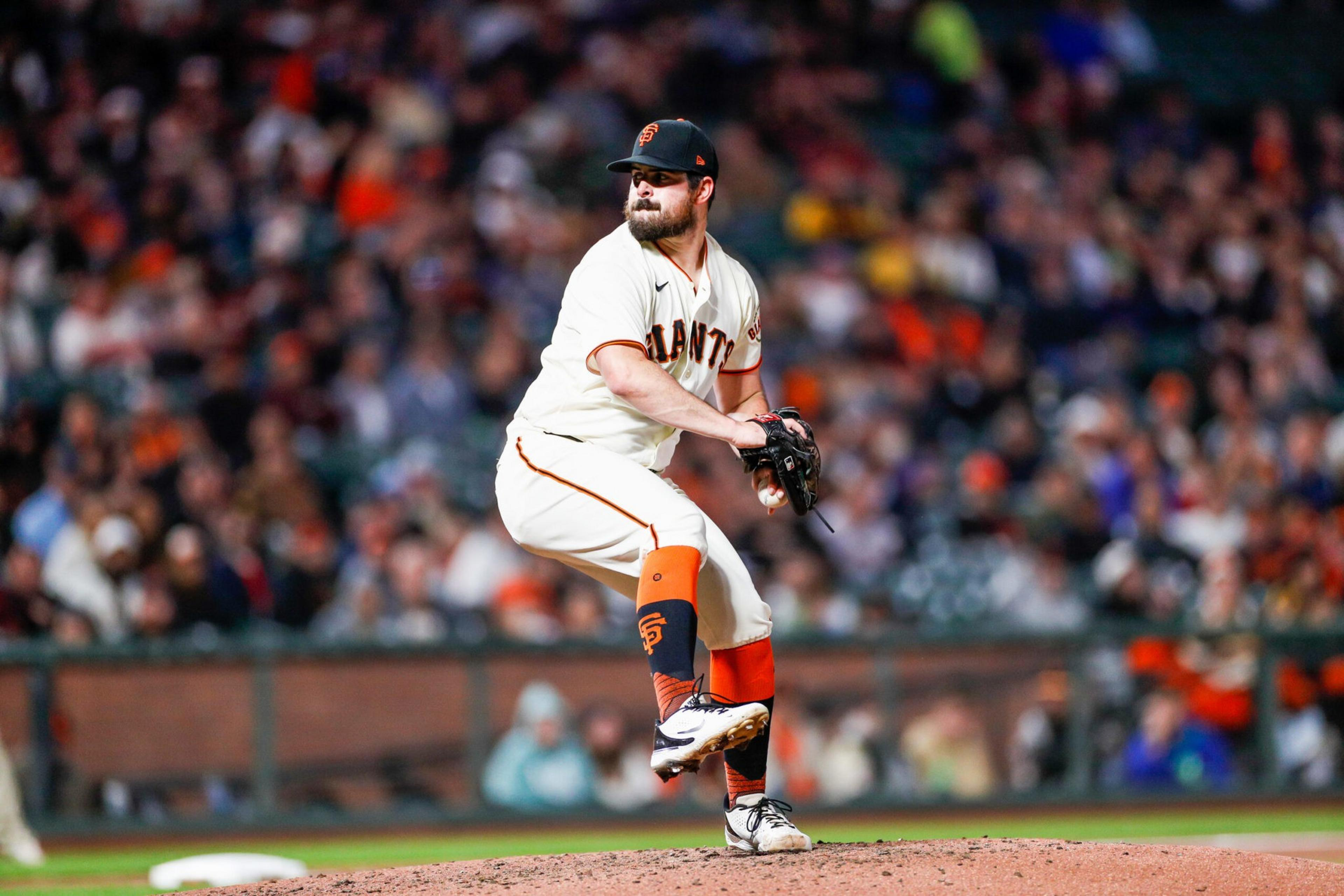A baseball pitcher in a San Francisco Giants uniform prepares to throw a pitch on the mound with a crowded stadium in the background.
