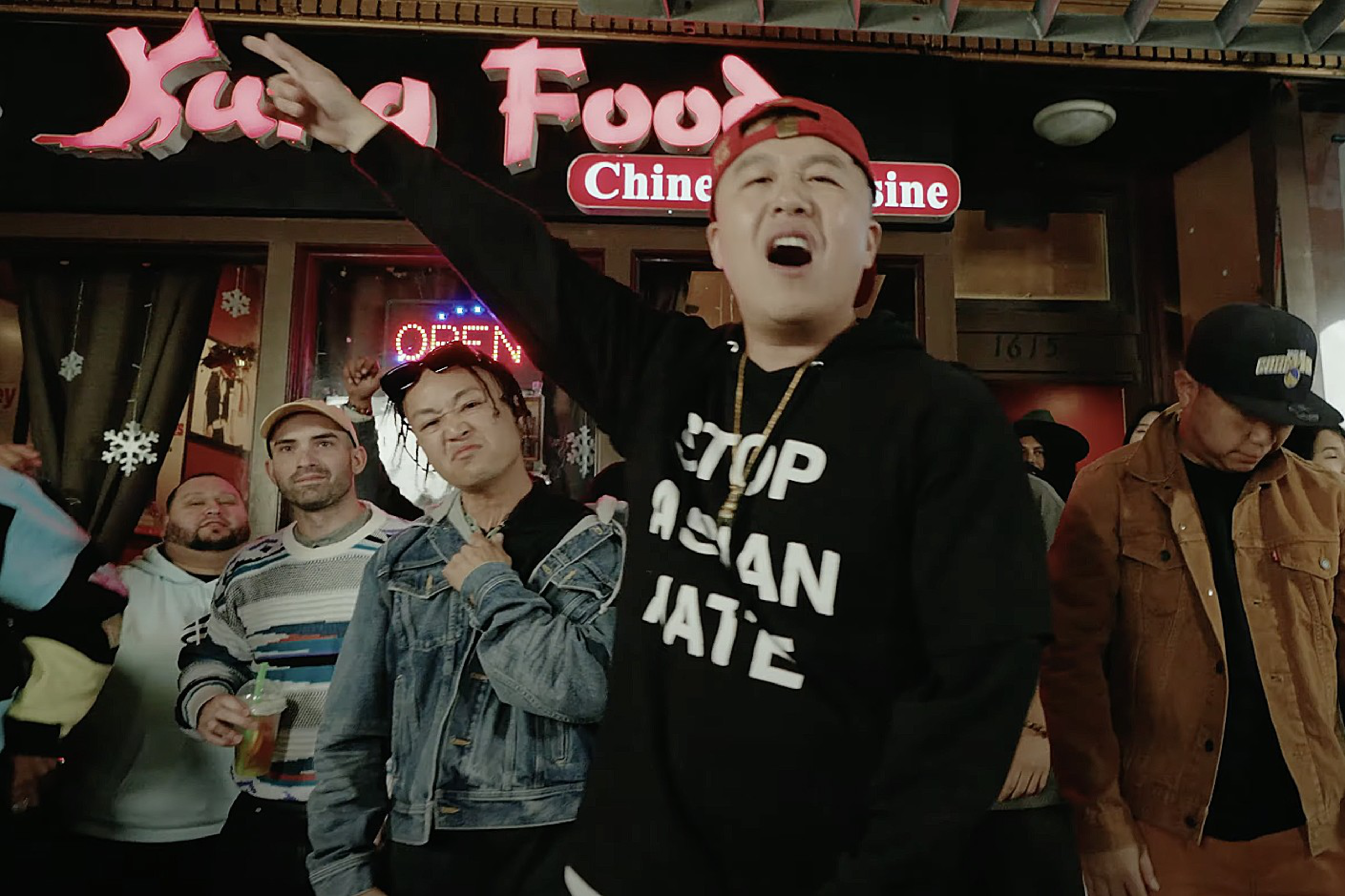 A man raps outside of a restaurant called Kung Food with people in the background.
