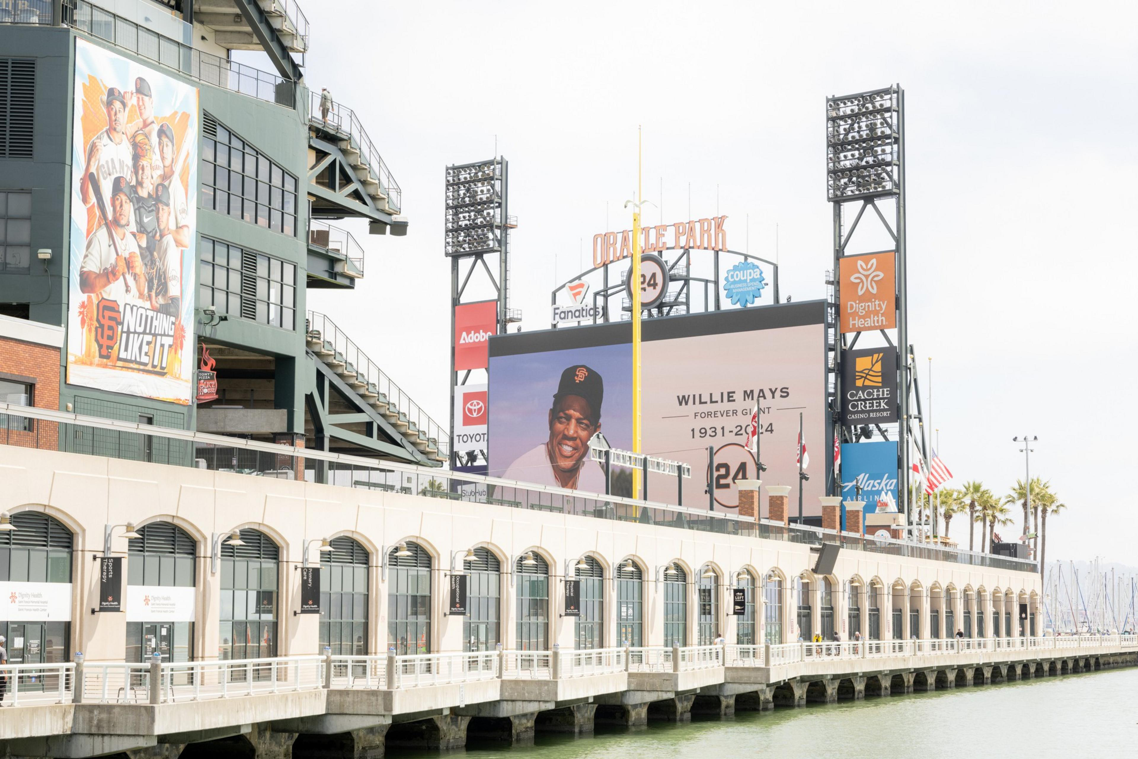 The image shows Oracle Park featuring tributes to Willie Mays, with large banners and signs, including his photo and the message &quot;Forever Giant, 1931-2024.&quot;