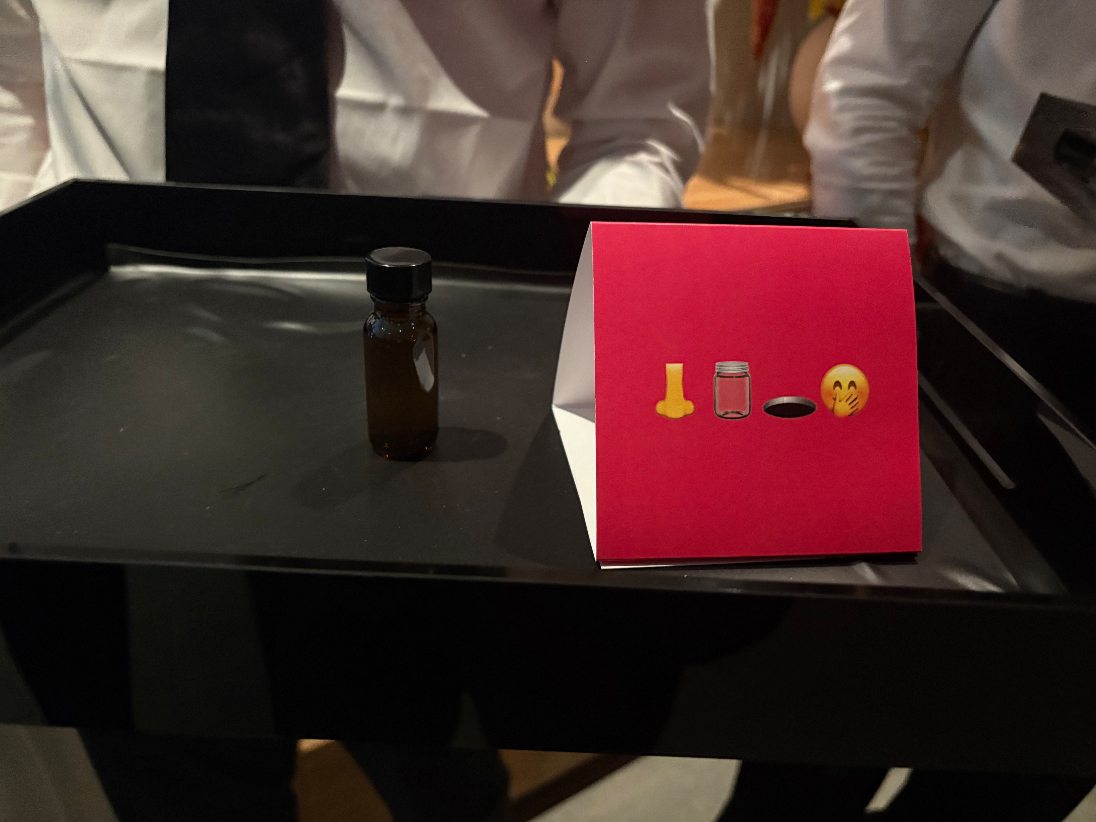 A small brown bottle with a black cap sits on a black tray next to a ...
