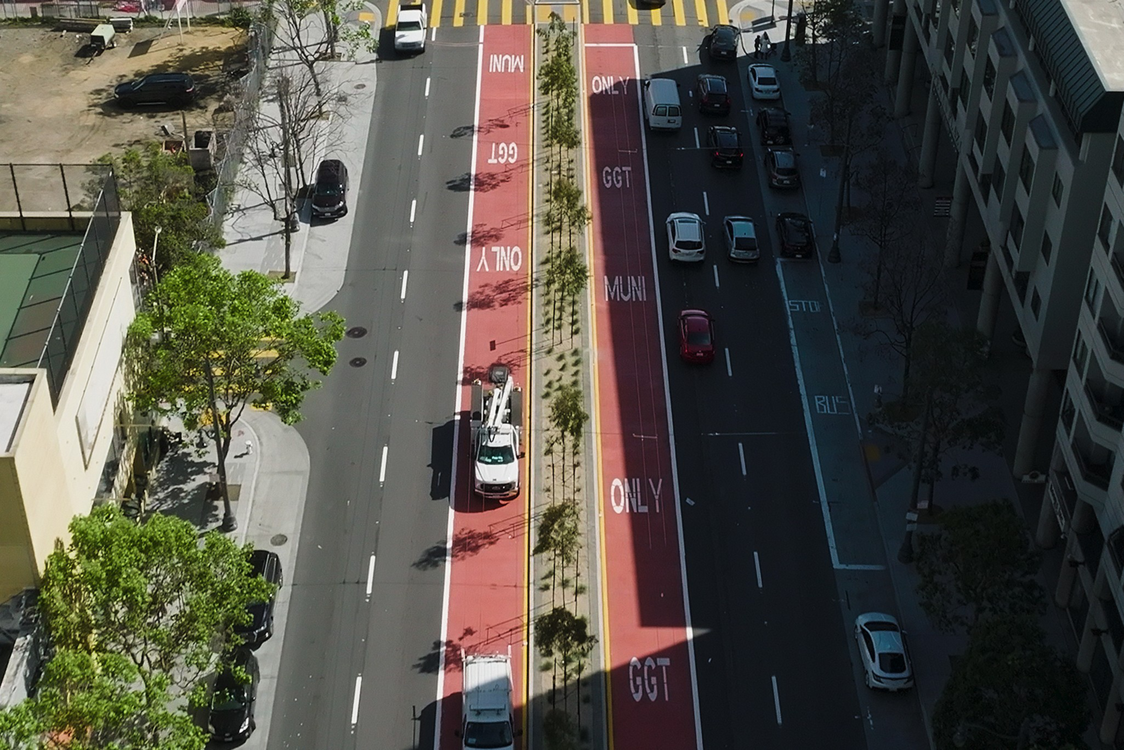 A multi-lane city street with red bus and transit-only lanes in the center, traffic moving in both directions, bordered by sidewalks and buildings.
